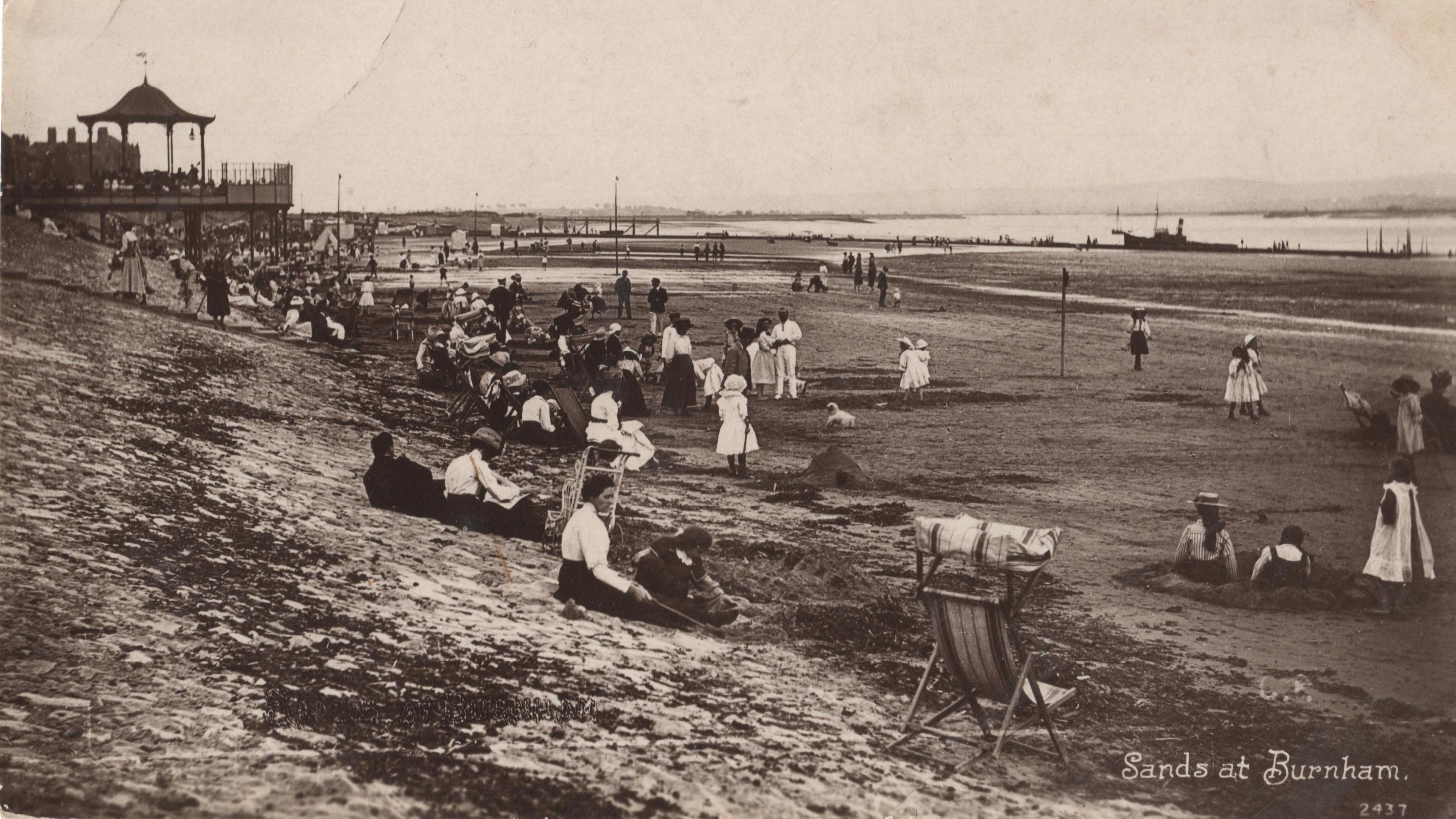 A Victorian photograph showing people on the beach at Burnham, with a few sitting on deck chairs