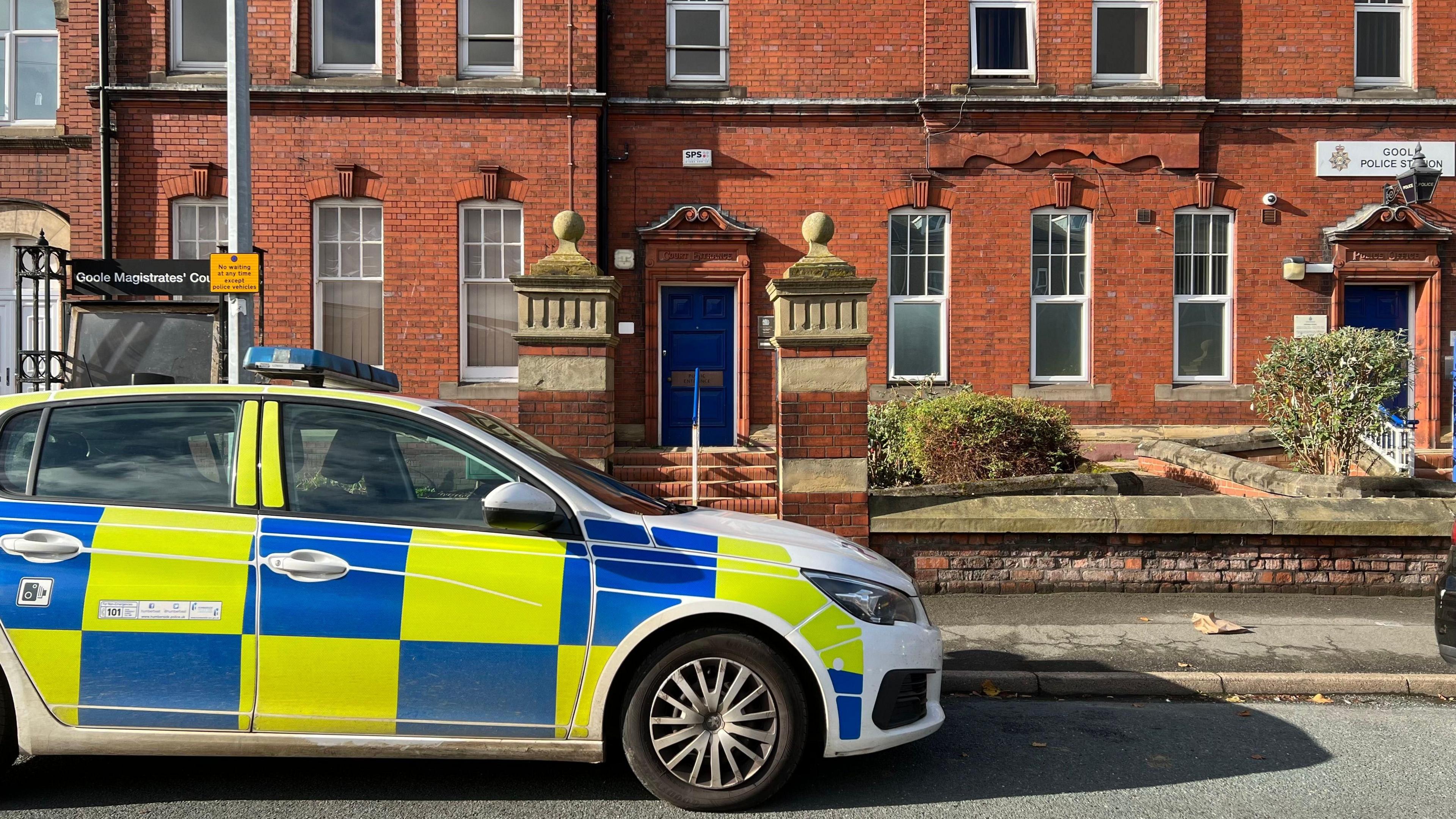 A police car parked outside a red-brick building in front of a blue door