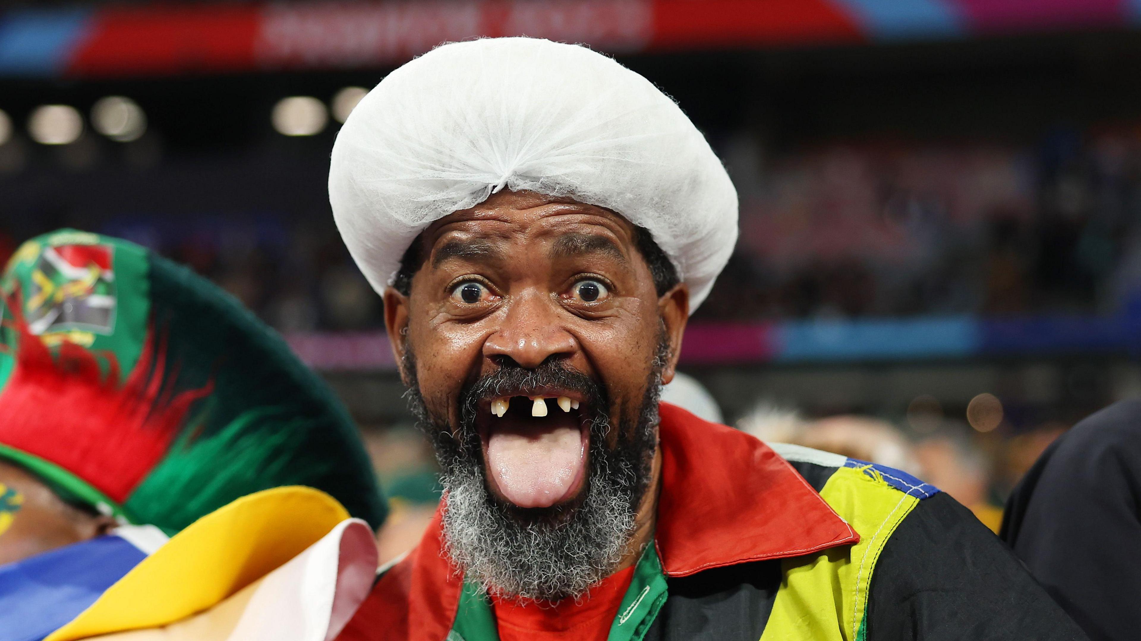 South Africa superfan in a stadium pokes his tongue out as he looks into the camera, showing off missing teeth