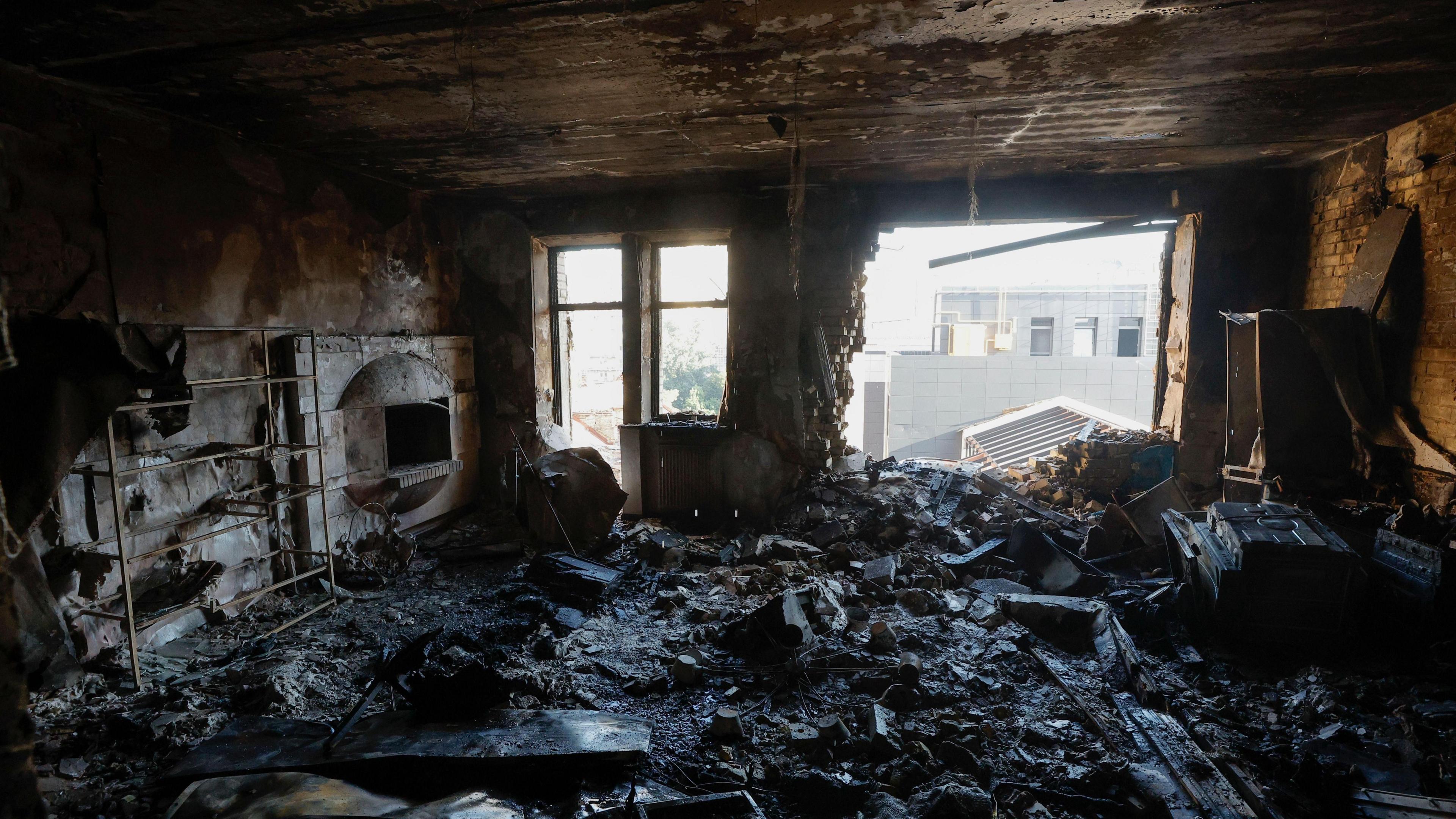 Rubble fills a burnt-out flat in Kyiv. Smashed windows leave the room open to the sunlight and charred wood and debris covers the floor.