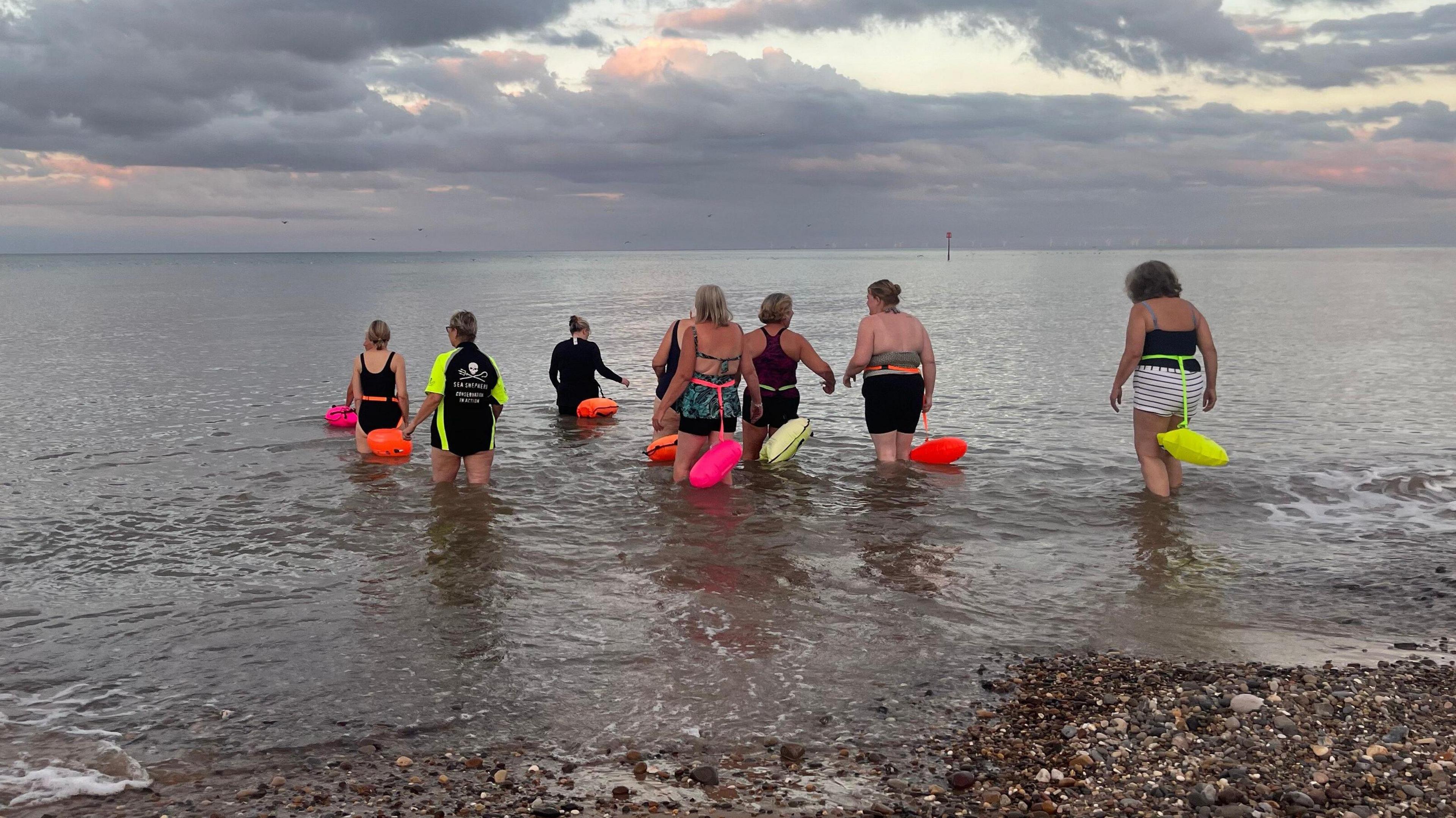 Eight women in swimming costumes and wearing fluorescent buoyancy aids walk into the sea for a swim and a natter.