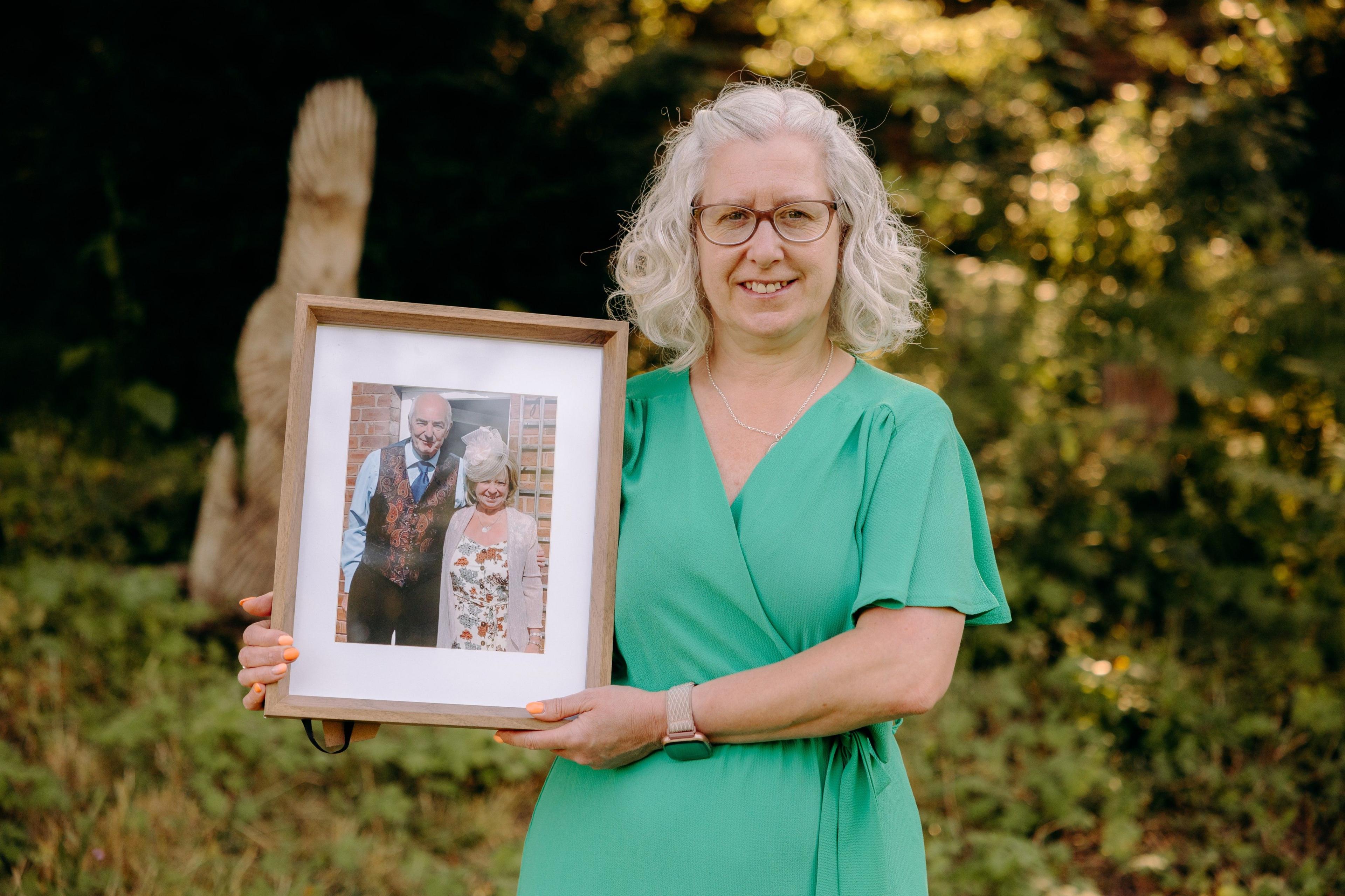 Woman in green dress holding up photo of her parents