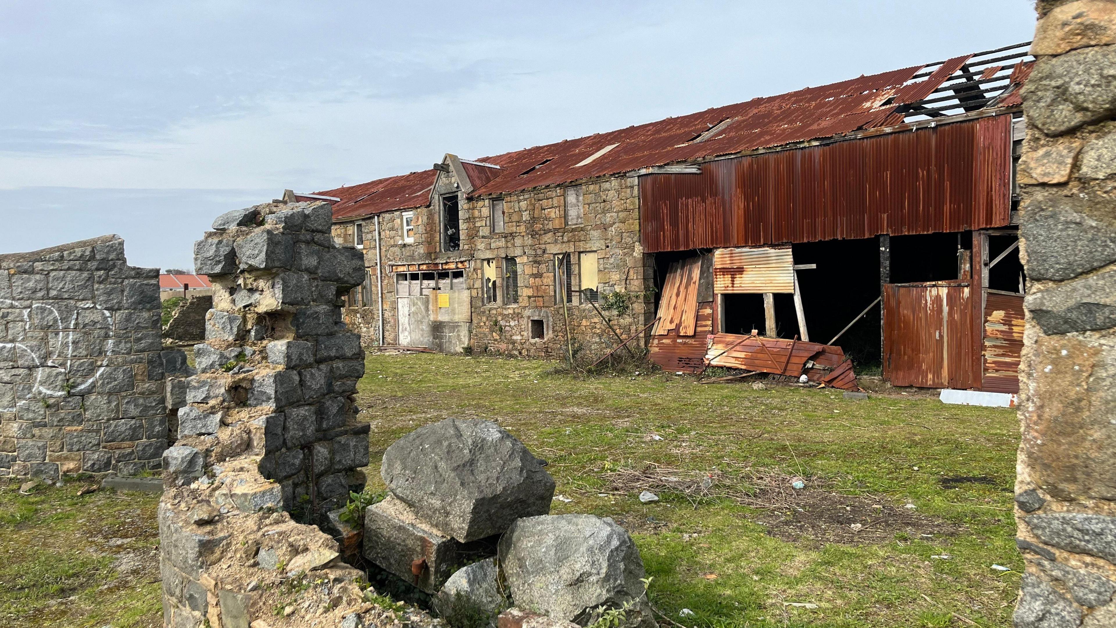 Crumbling brick walls in front of a derelict building with rusted corrugated iron walls. 