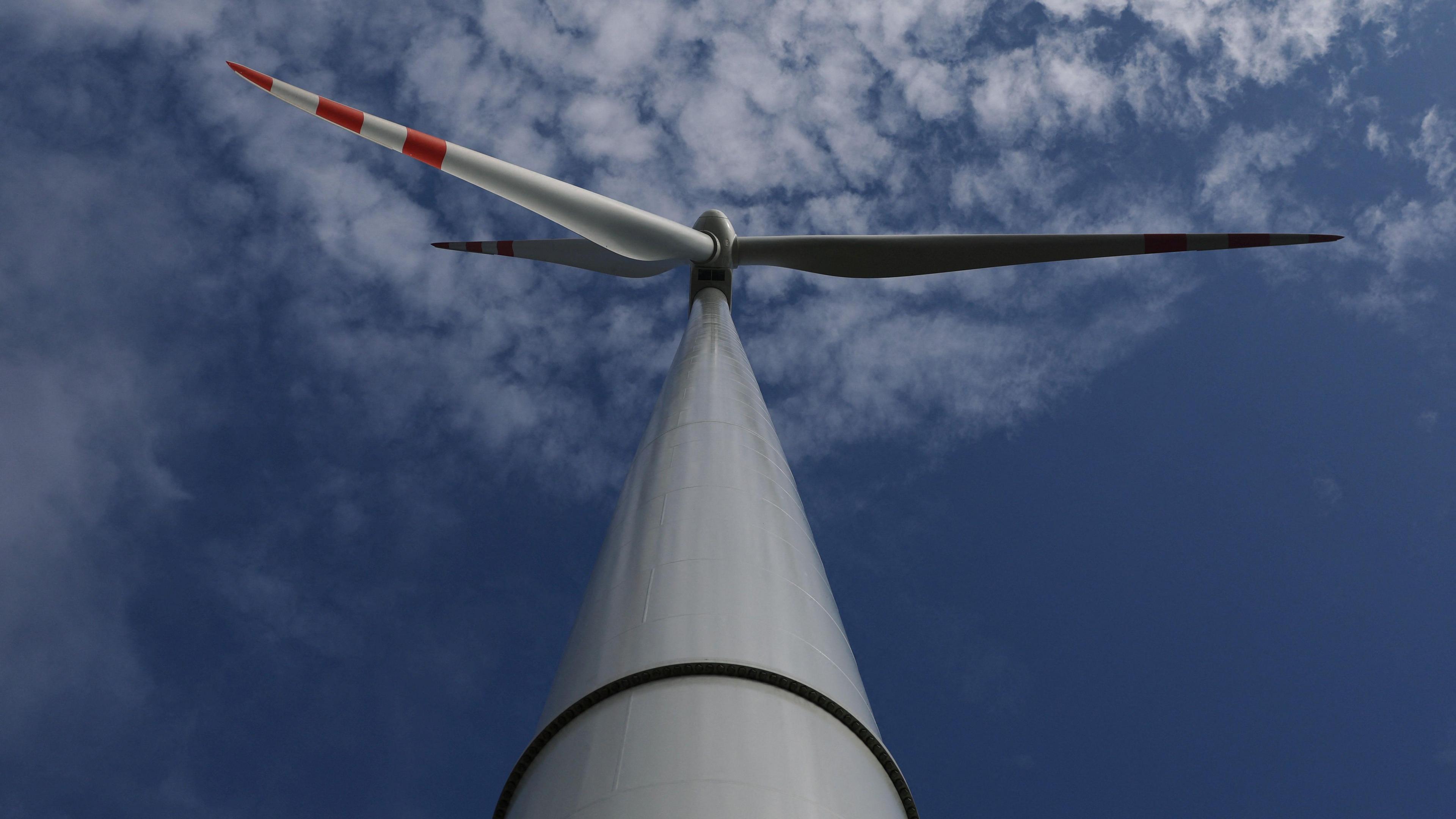 A wind turbine tower and blades viewed from the ground looking up into a blue sky with light clouds