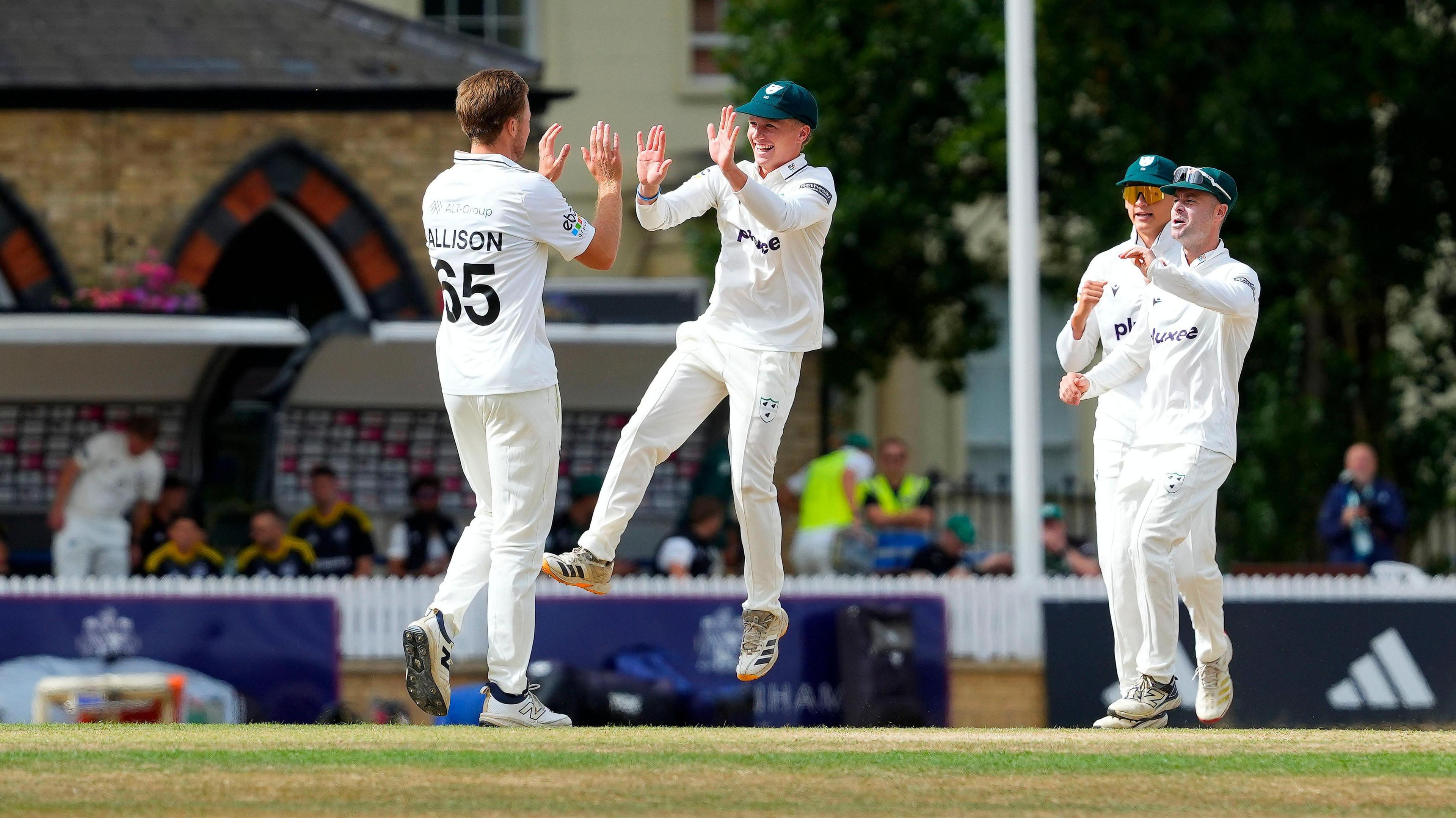 Ben Allison (left) holds two palms up as a team-mate jumps in the air towards him in celebration of a wicket