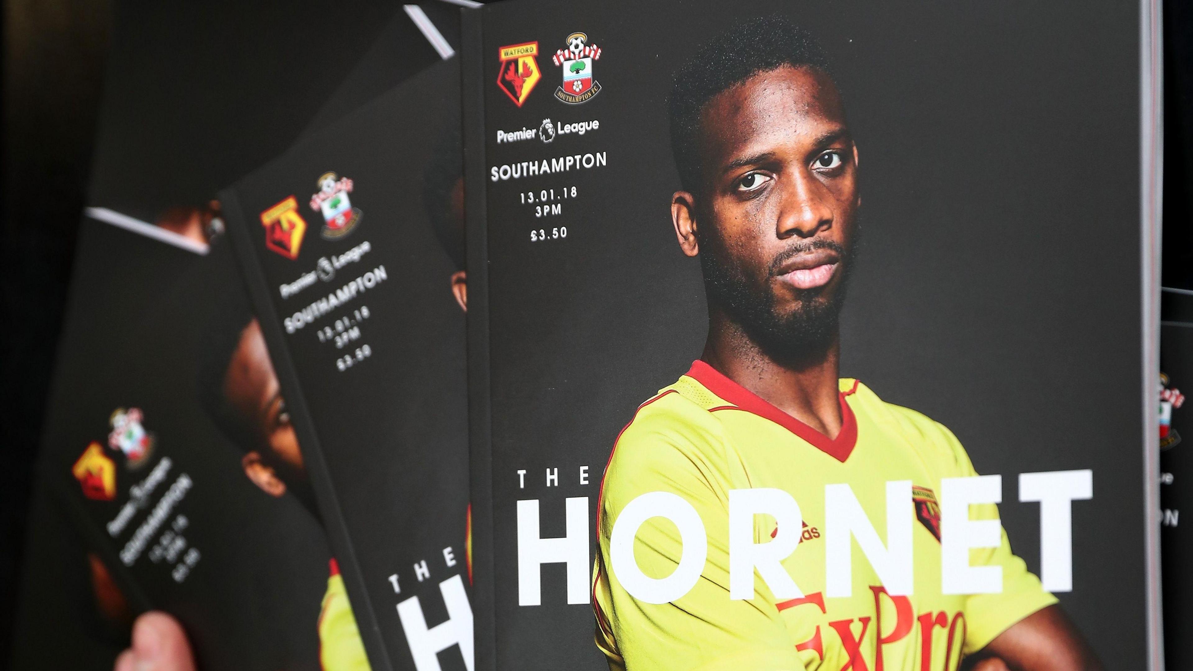 A scattered pile of football programmes featuring a player in a yellow and red kit with arms crossed on the cover.