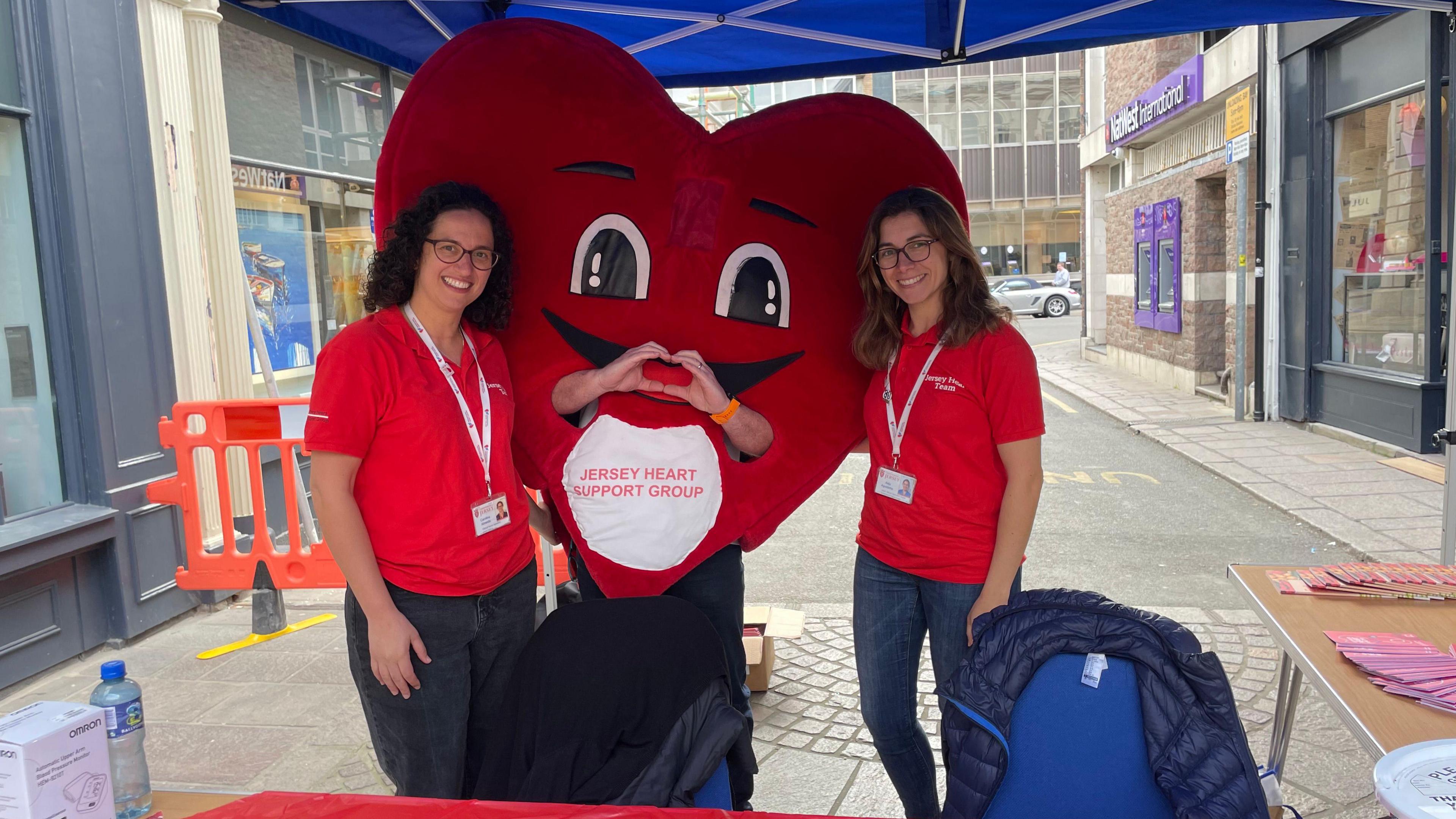 Two women in red polo shirts and a big red heart mascot
