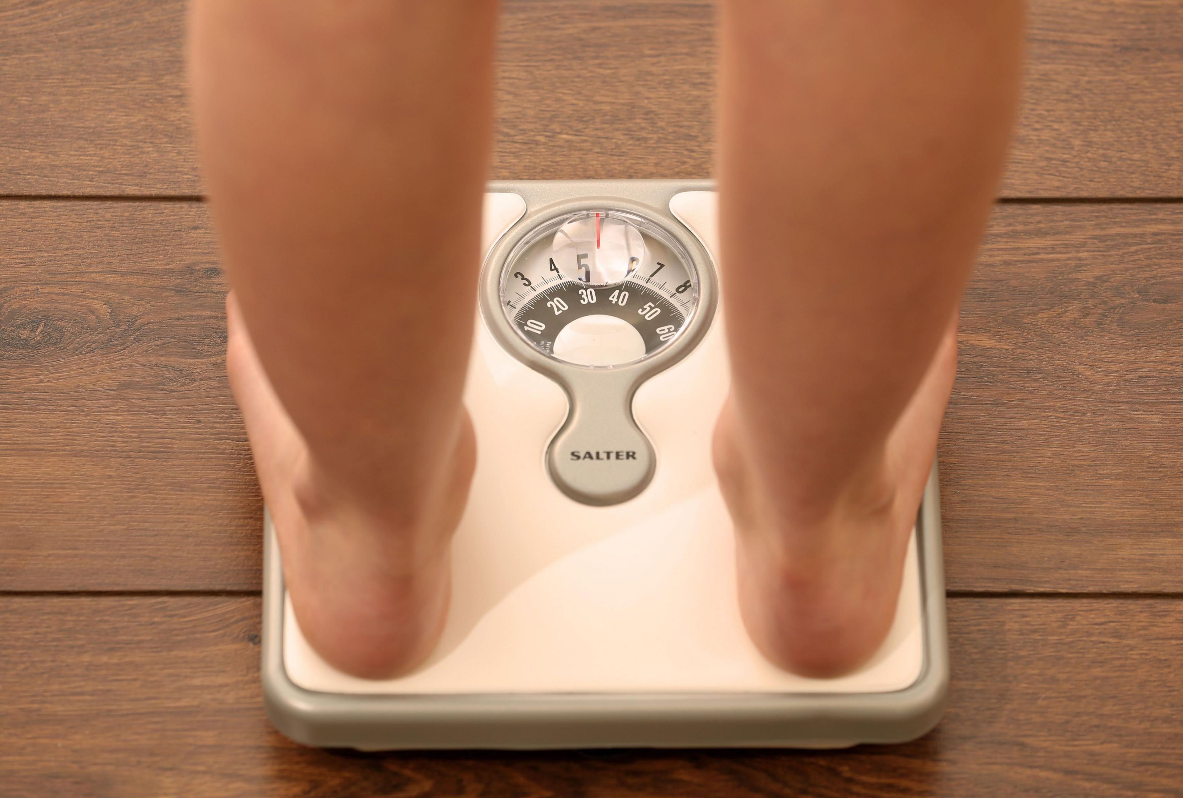 A stock image of a person standing on a set of scales. Only the bare feet are visible.