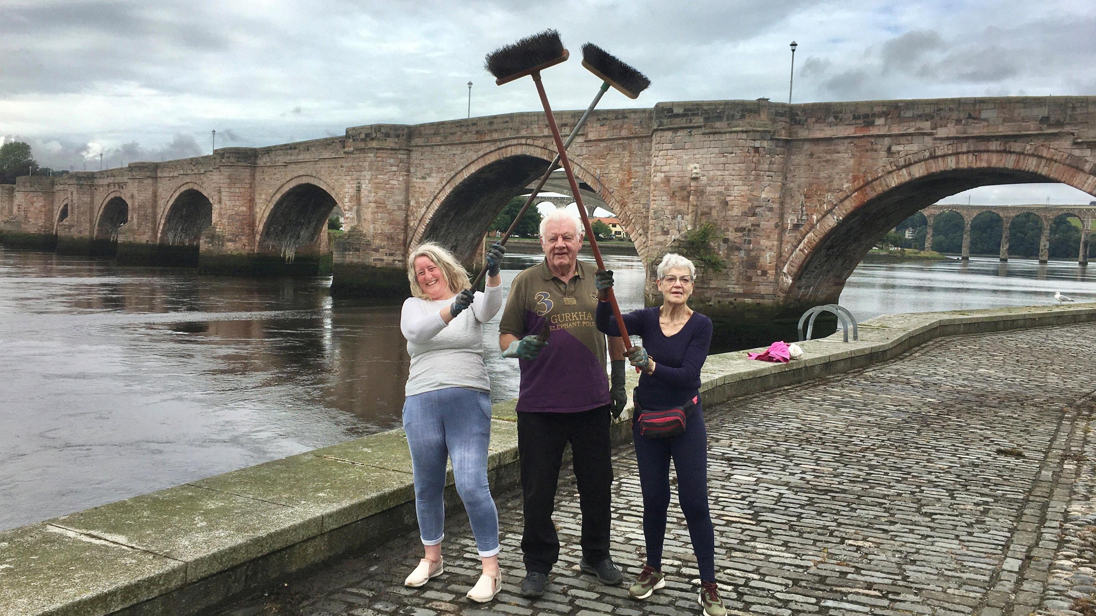 Lindsay Benton, Canon Alan Hughes and Margaret Shaw hold their brushes up with the bridge in the background