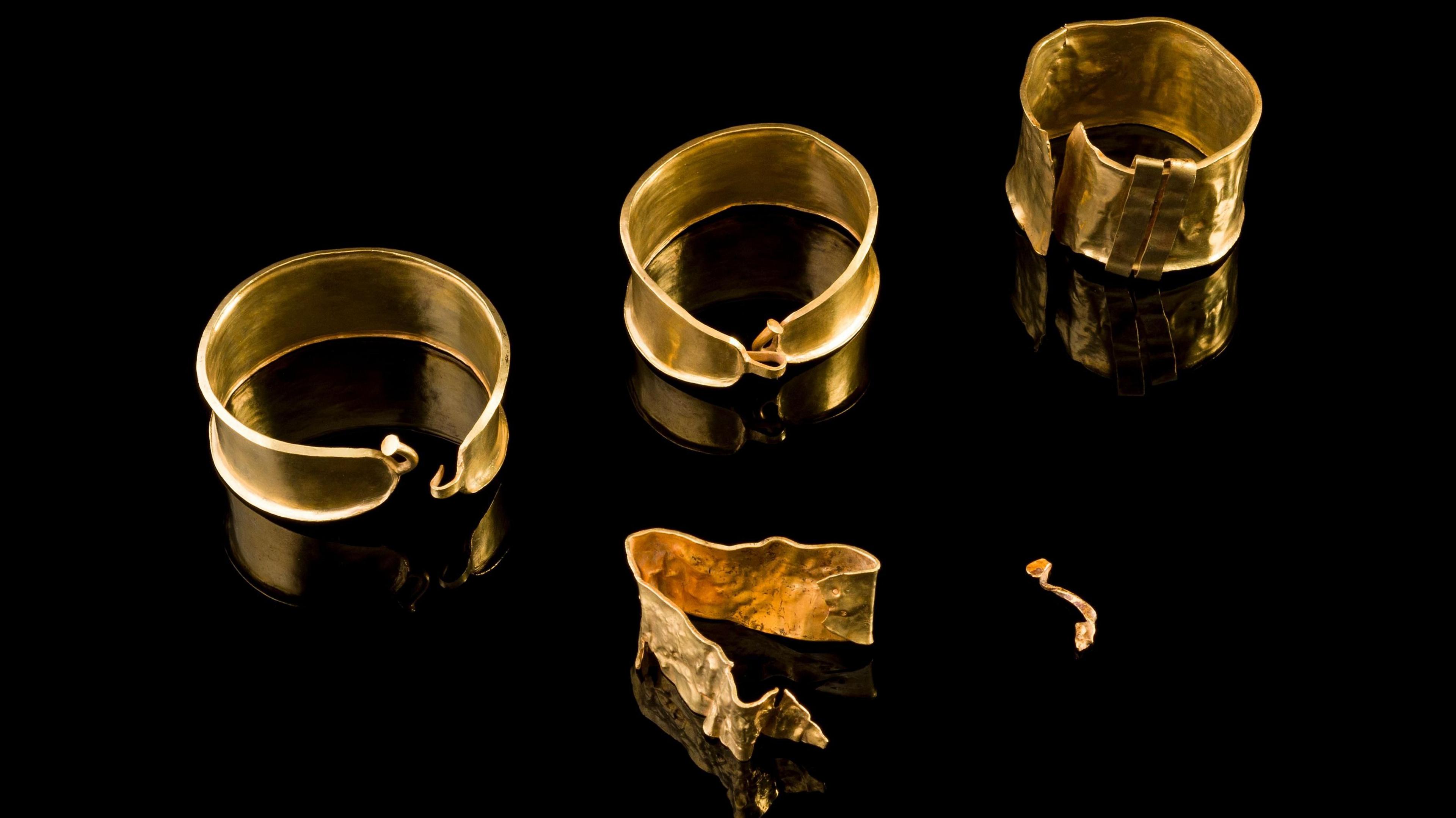 Gold jewellery dating back to the Bronze Age laid out on a black surface.