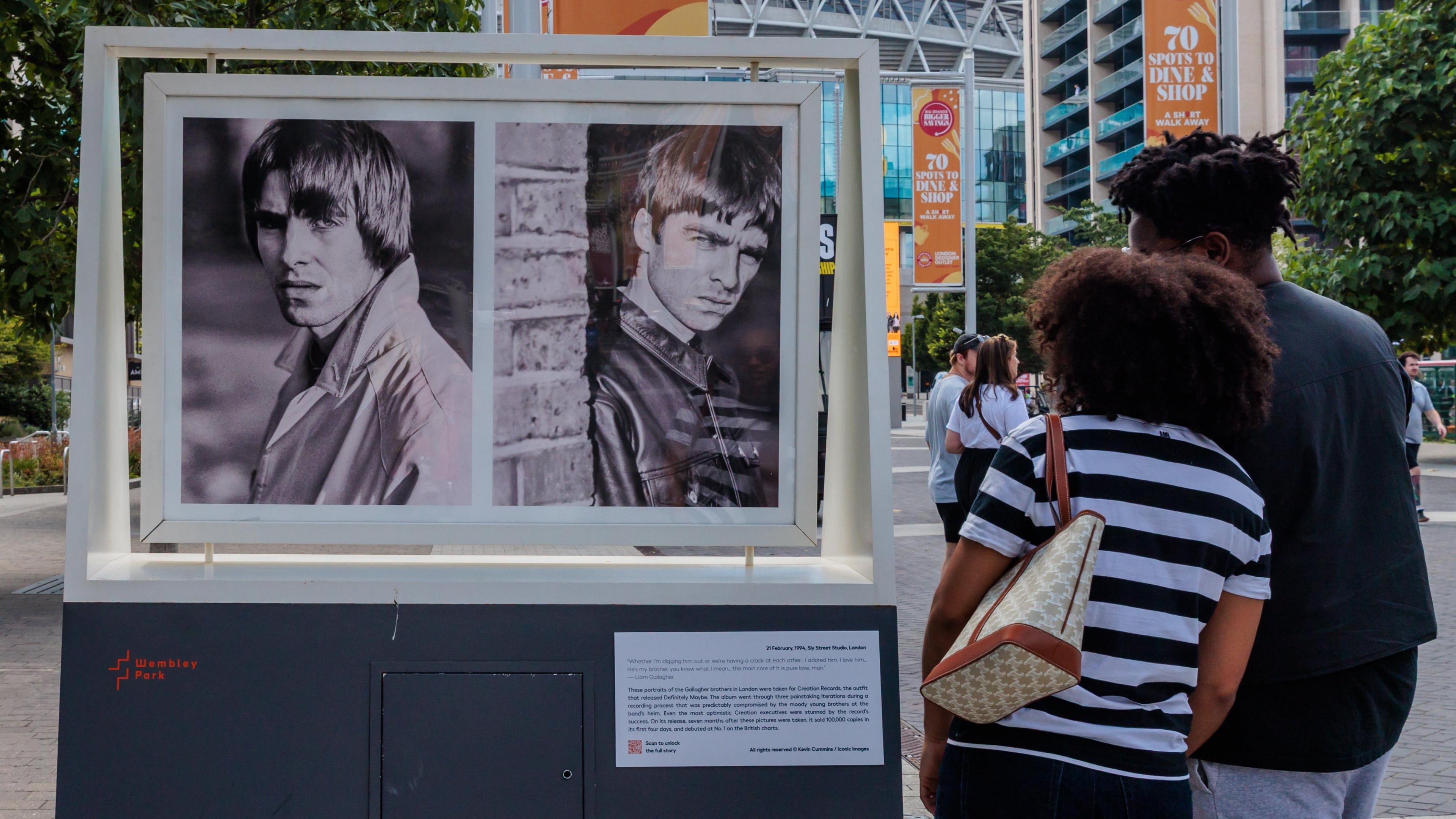 two people look at two black and white photos of the Oasis duo in the exhibition