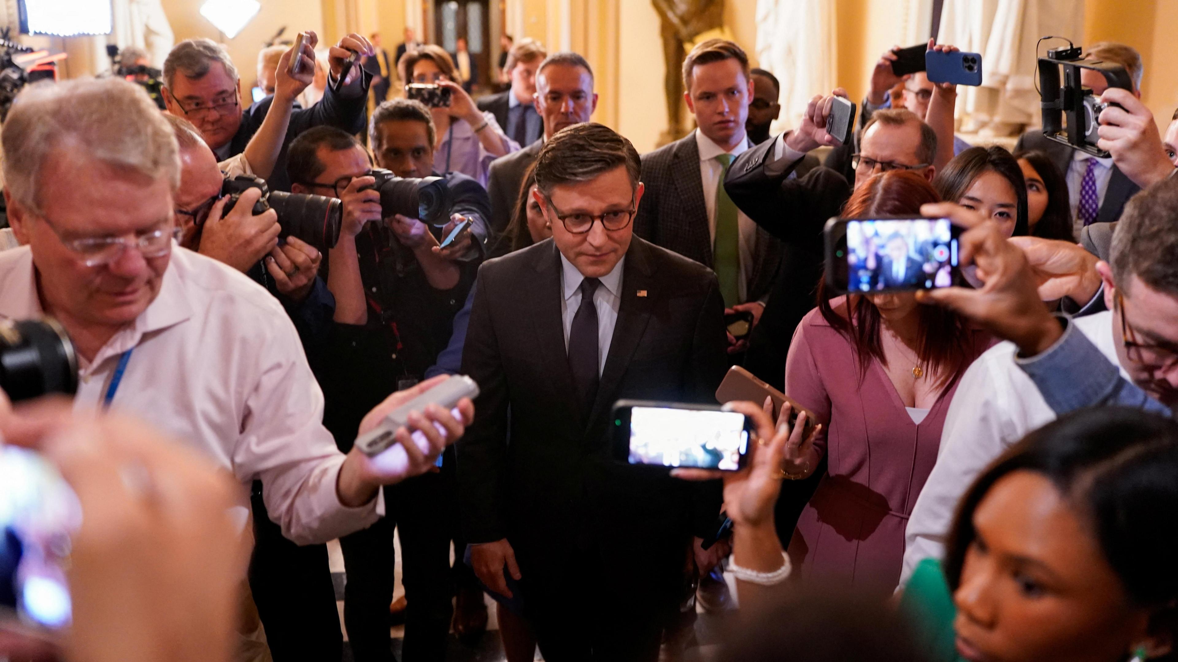 Mike Johnson walking on Capitol Hill surrounded by reporters holding cameras and cell phones.
