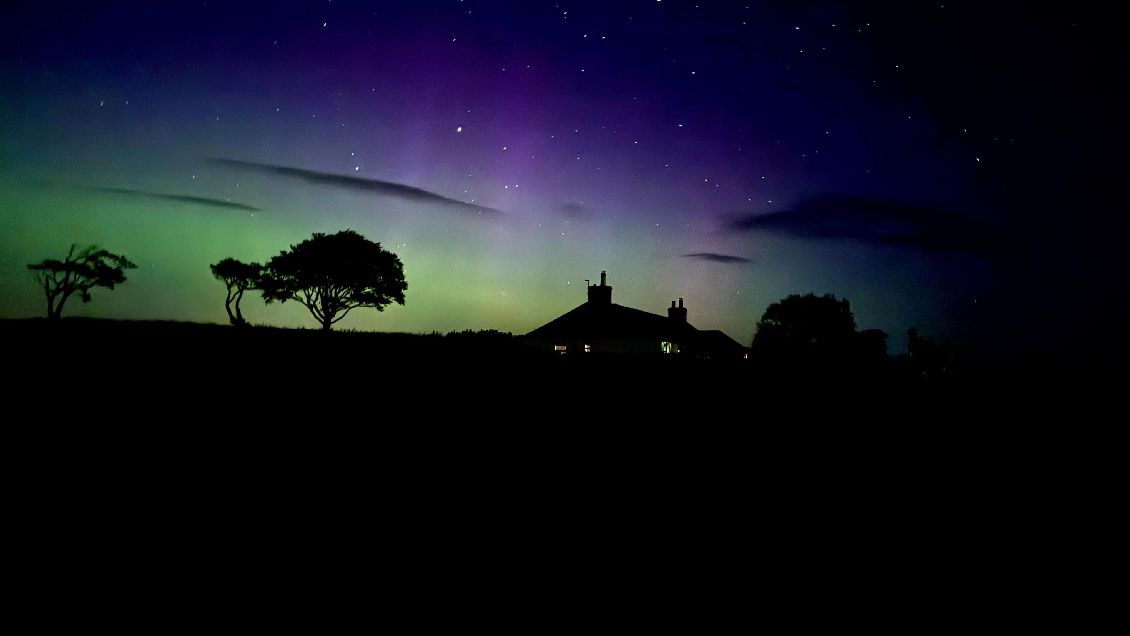 Silhouette of a house and trees against the green purple and blue night's sky in Fife, Scotland