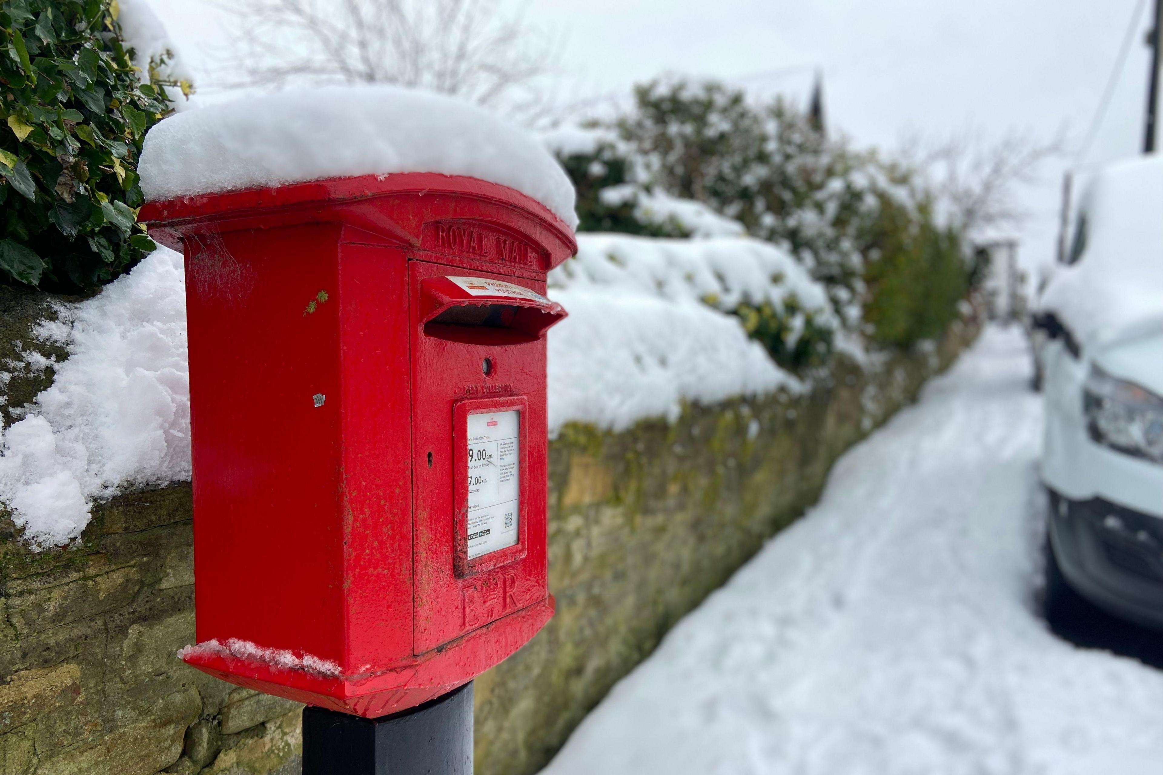 A red postbox with a thick layer of snow on top of it