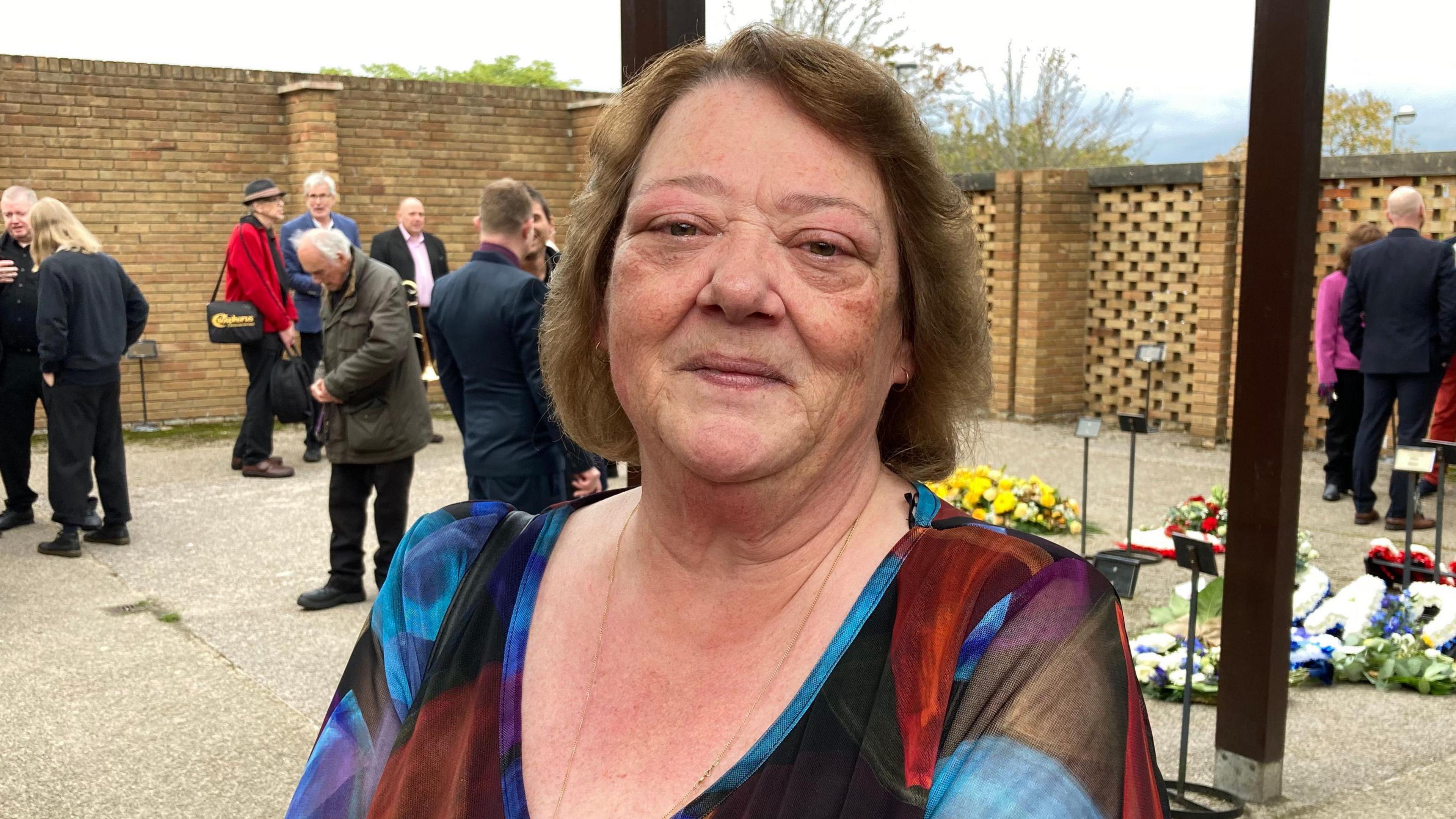 Maria Huggett smiling at the camera with her hair in a bob wearing a colourful top at the funeral