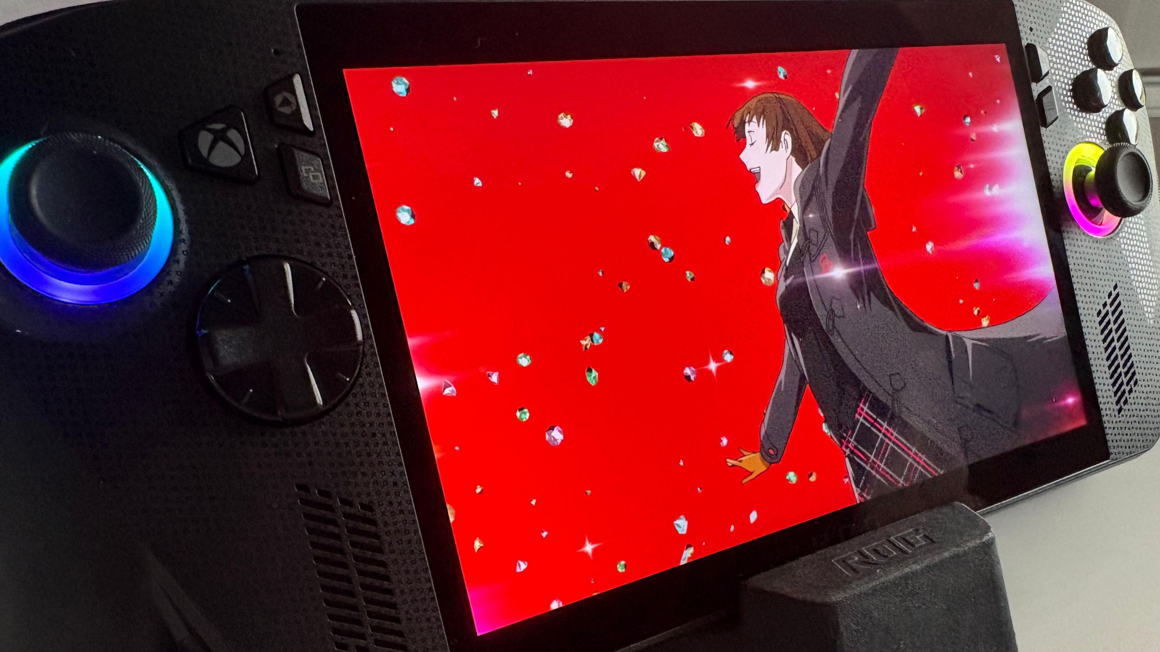 The Xbox handheld on a black stand against a white background. It is at a slight angle focusing on the left-hand side of it. On the screen, a cutscene from Persona 5 Royal. It is a bright red colour with an anime character running with her arms out. She has brown hair and is wearing a Japanese school uniform, with a jacket and gloves over the top. Around her, brightly-coloured diamonds appear to be falling against the red background.