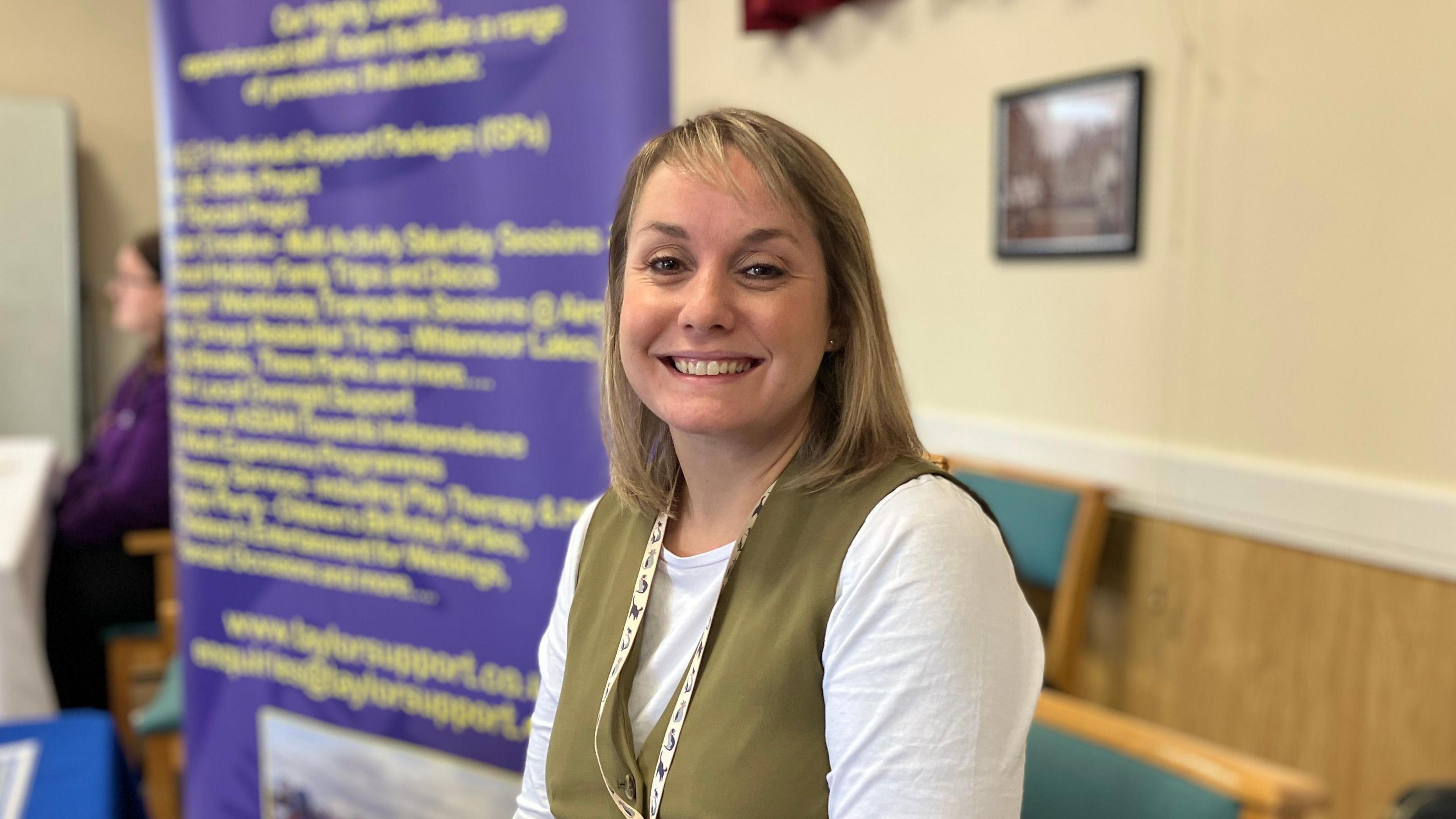 Business owner smiling sat down at jobs fair with purple pull up banner behind her.