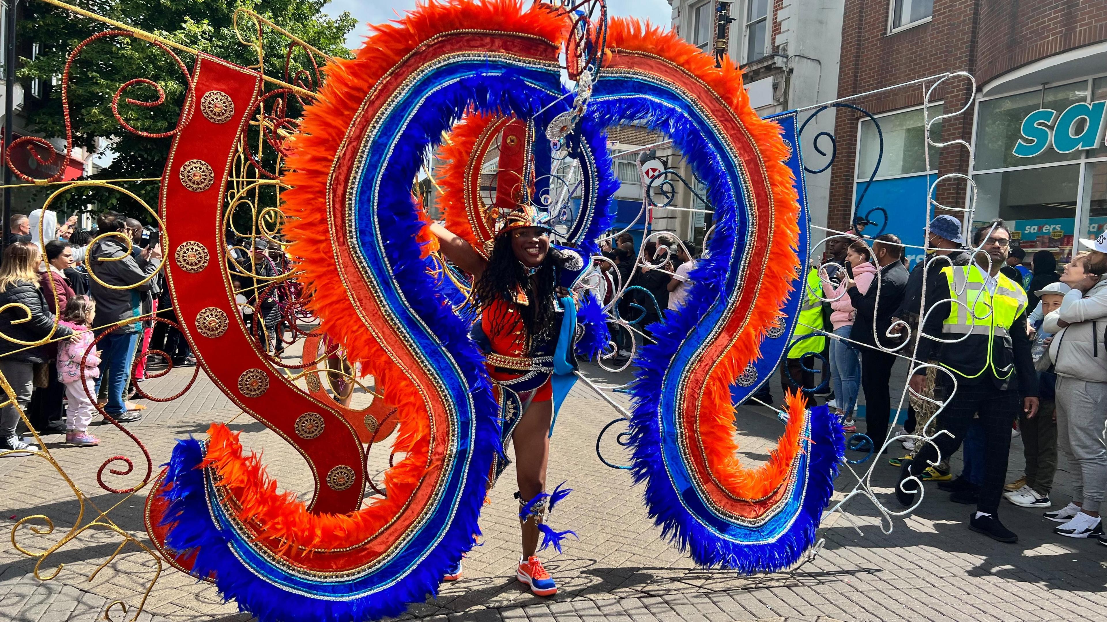 A woman wearing a colourful costume is surrounded by spectators on the street at Luton Carnival.