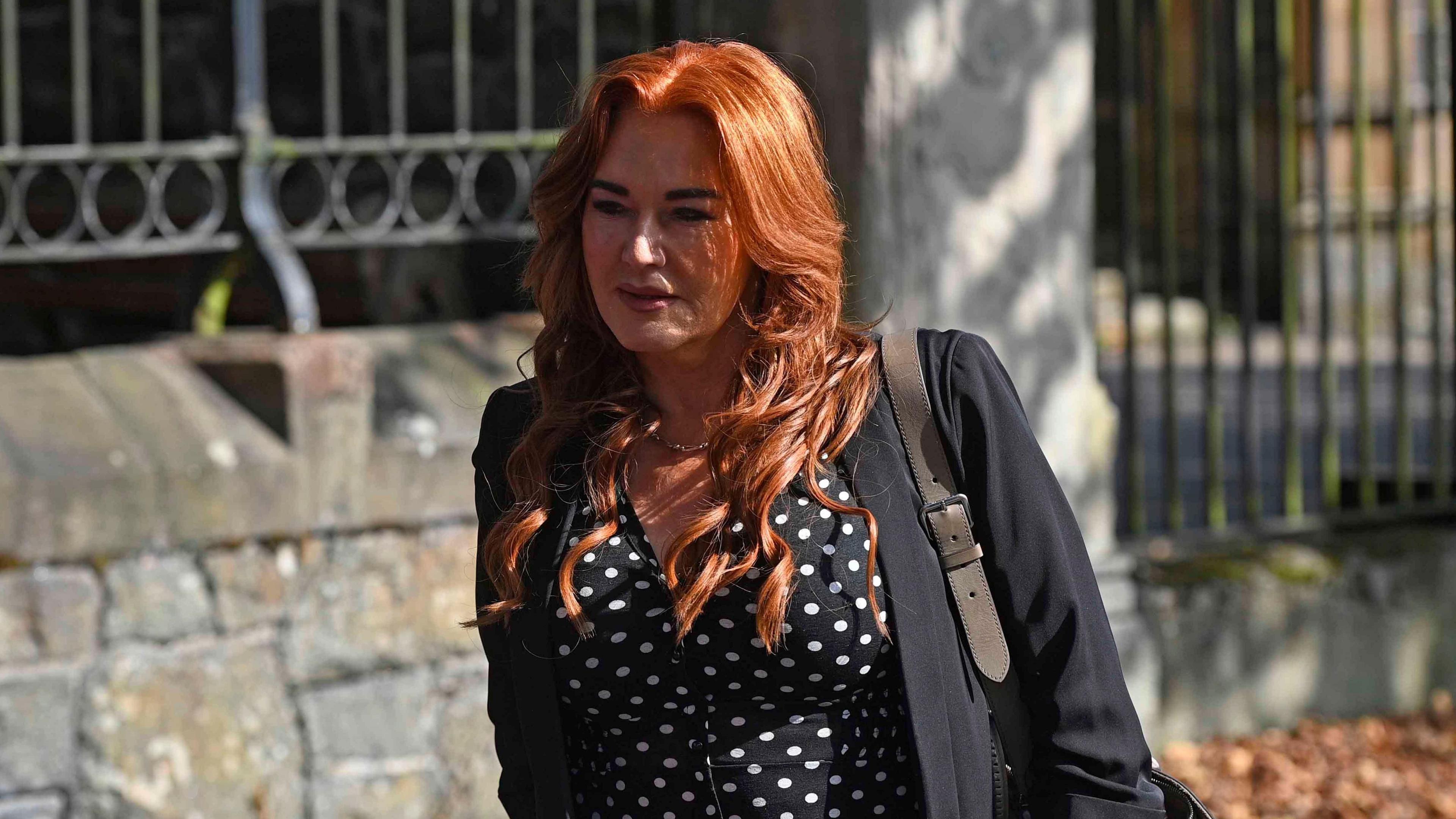 Anne Donaghy, a woman with red hair, wearing a dark jacket, and black blouse with white spots.