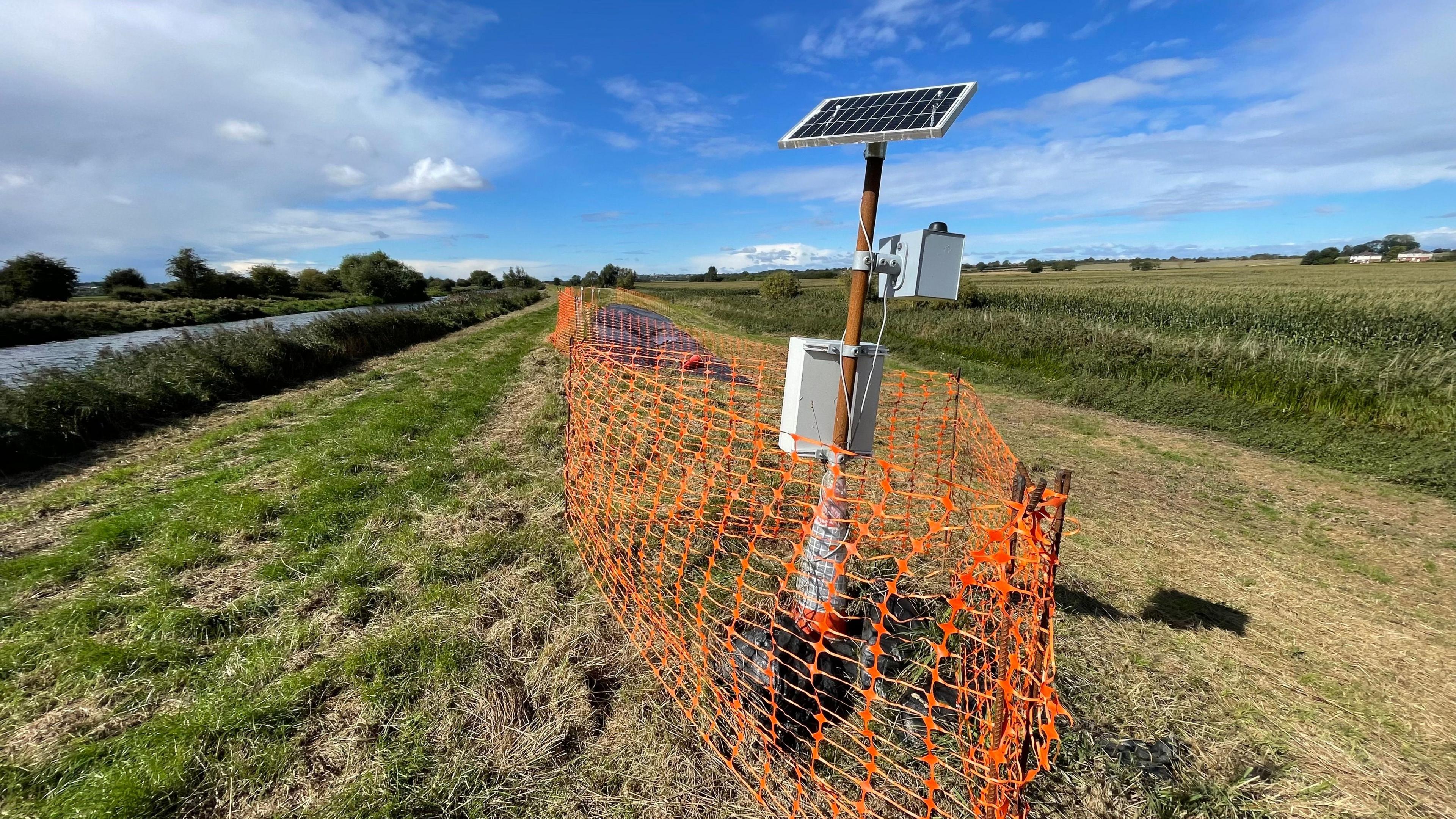 Monitoring equipment on the riverbank at Fiskerton. A pole has a solar panel at the top used to the power the equipment below. 