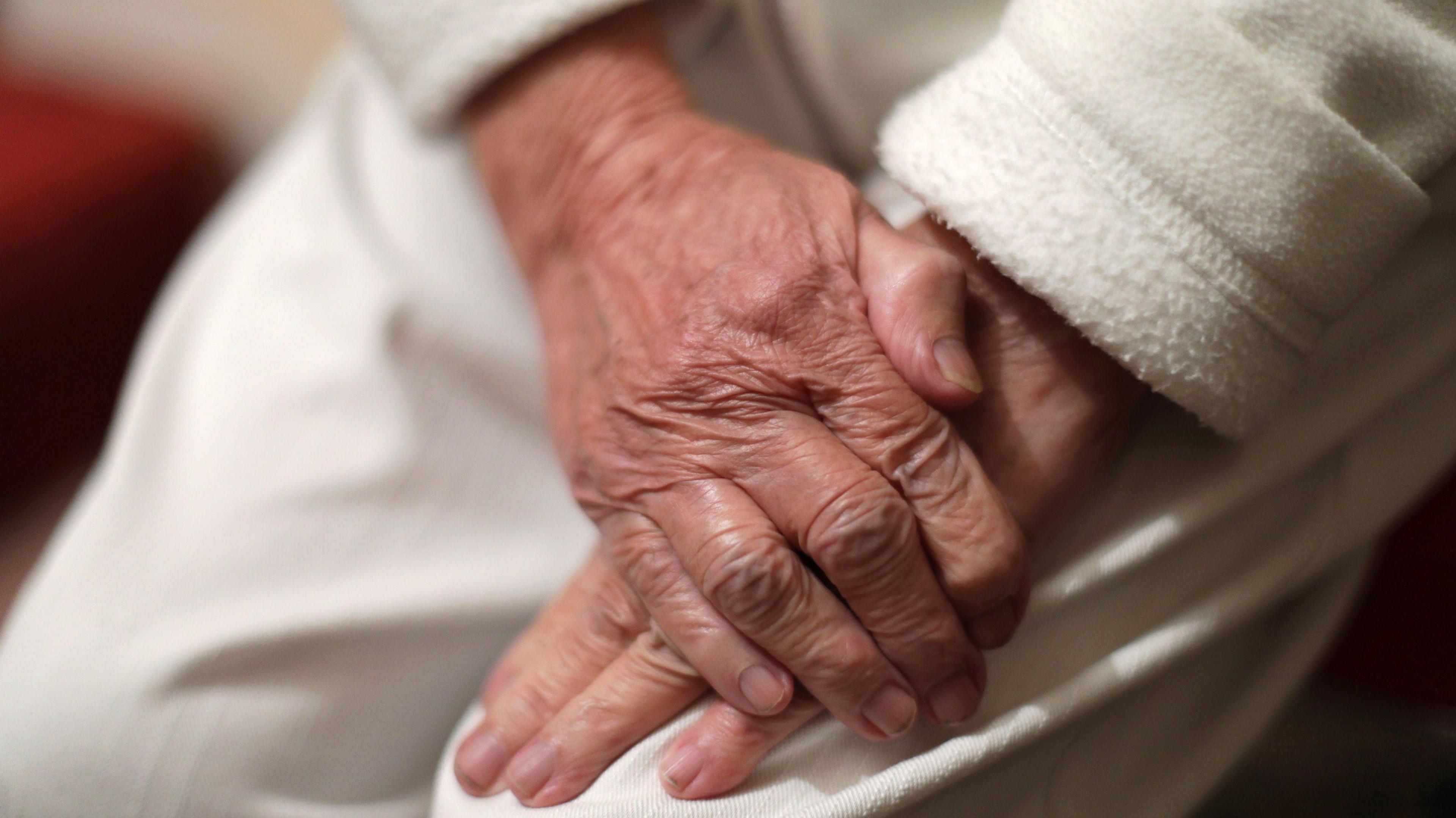 An elderly person clasps their hands together 