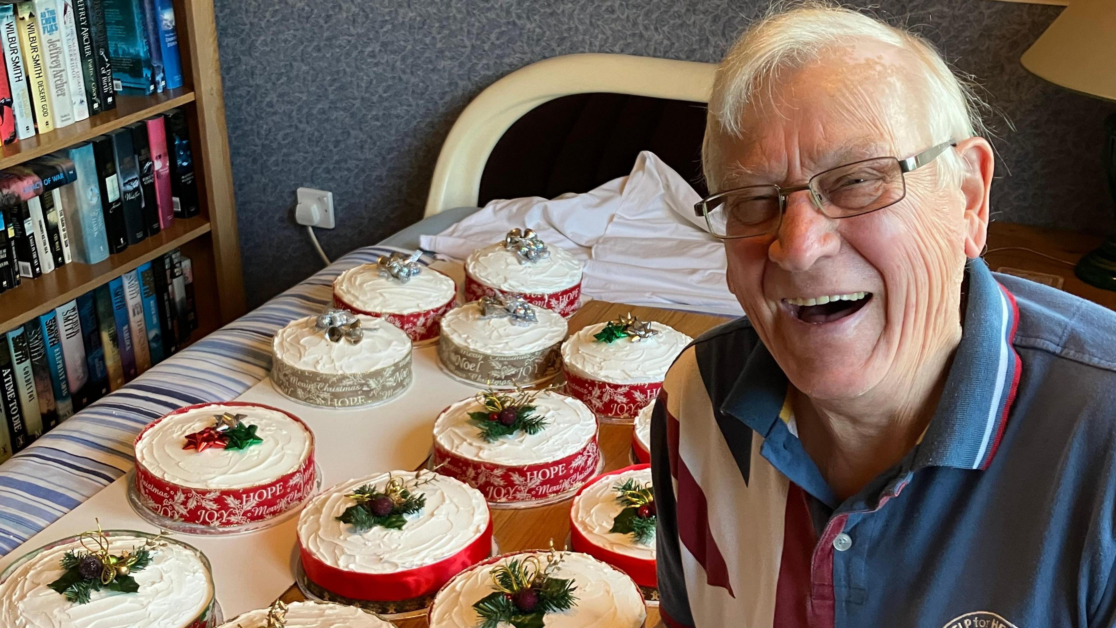 Baker David Brown, wearing glasses and a Help for Heroes shirt, sits next to a table covered with Christmas cakes decorated with festive toppings