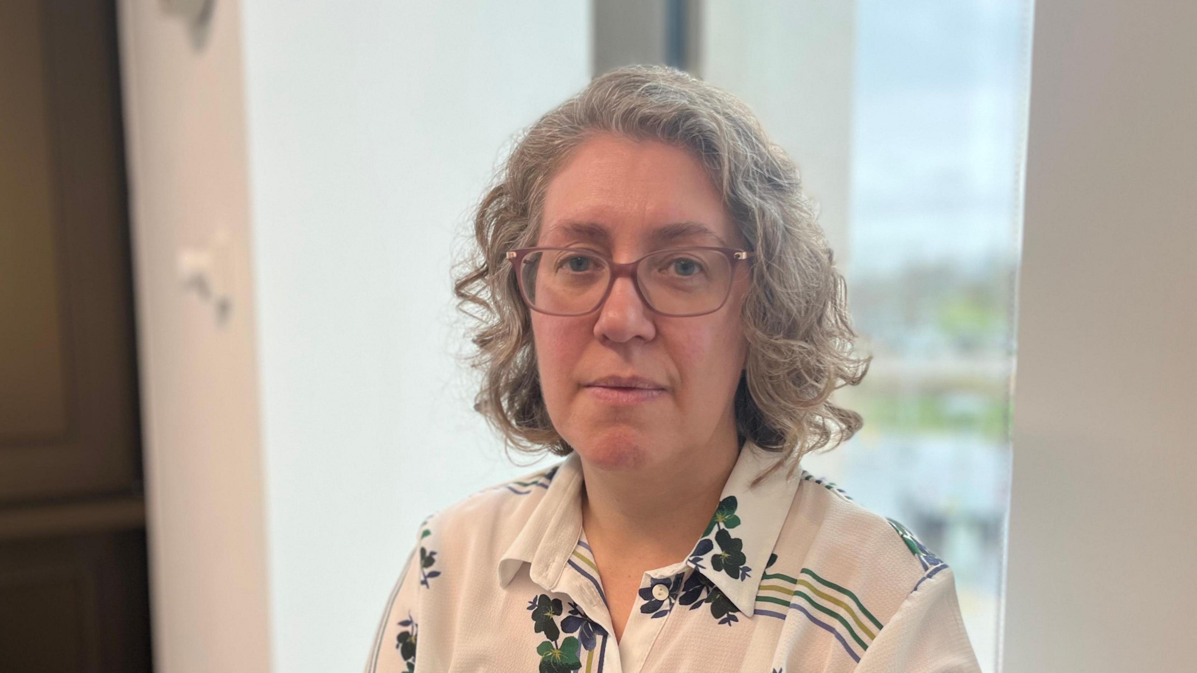 Prof Laura Machin, a woman with short, wavy fair hair and glasses, pictured in front of a window of a tall building.