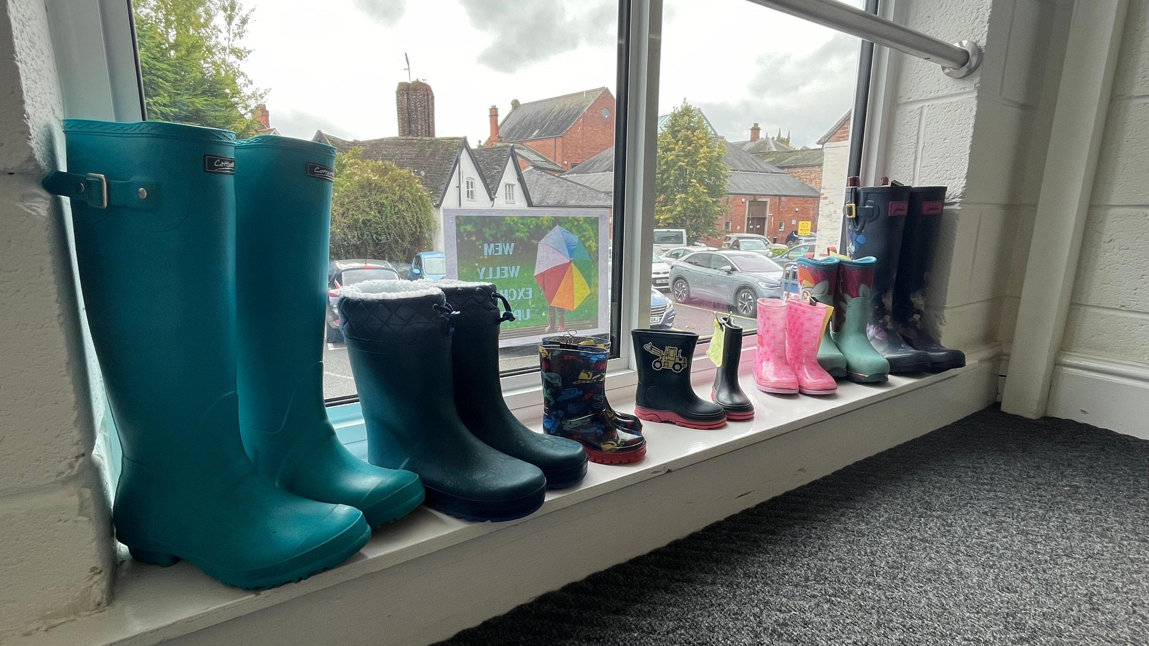 Seven pairs of wellies of varying sizes and colours lined up on a windowsill