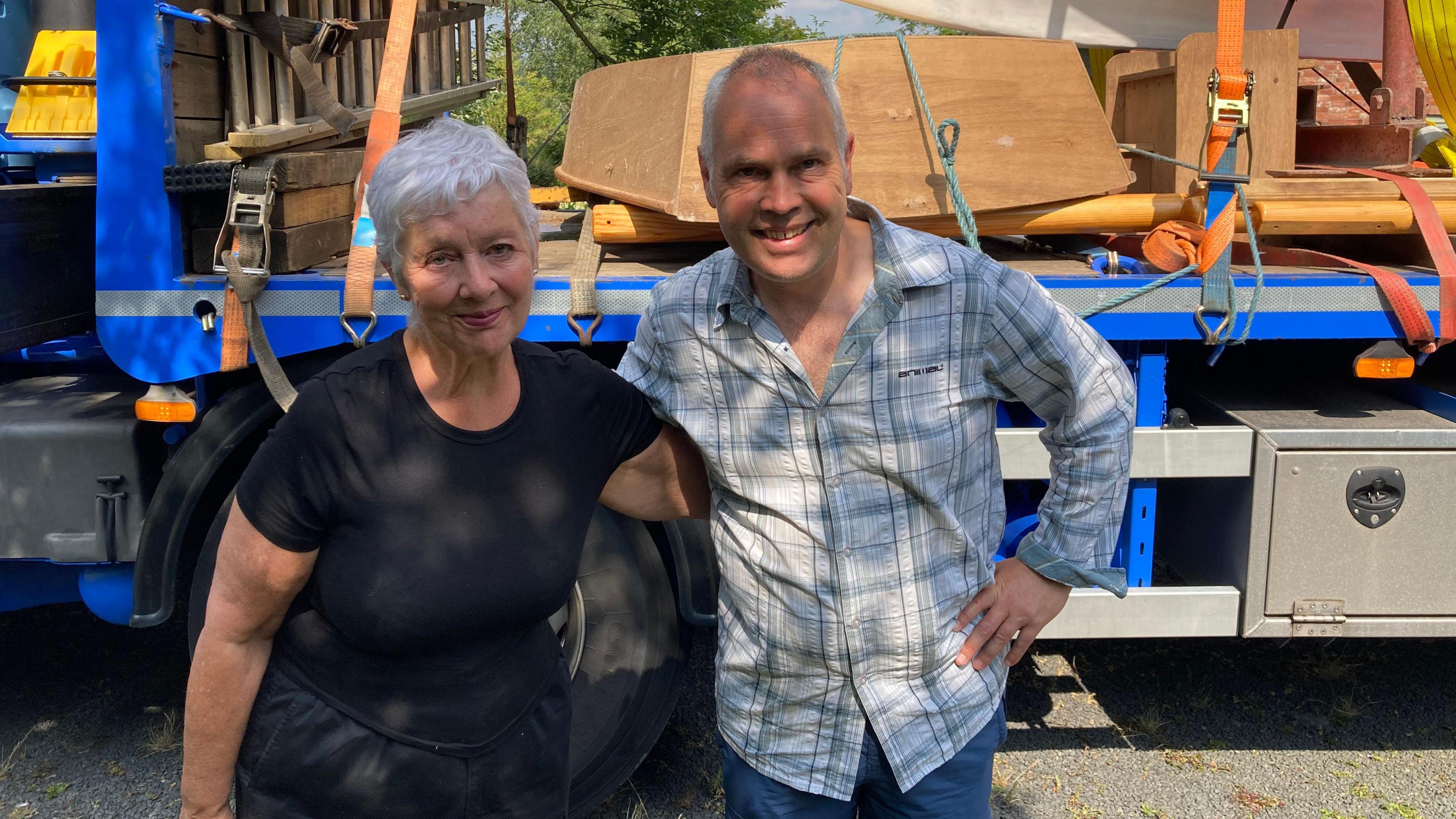 Anna Kaye poses with her arms around her son Jonathan Allen in fron of a trailer taking a boat away. They are smiling in the sunshine. She wears a blue t-shirt and Mr Allen wears a light blue checked shirt.