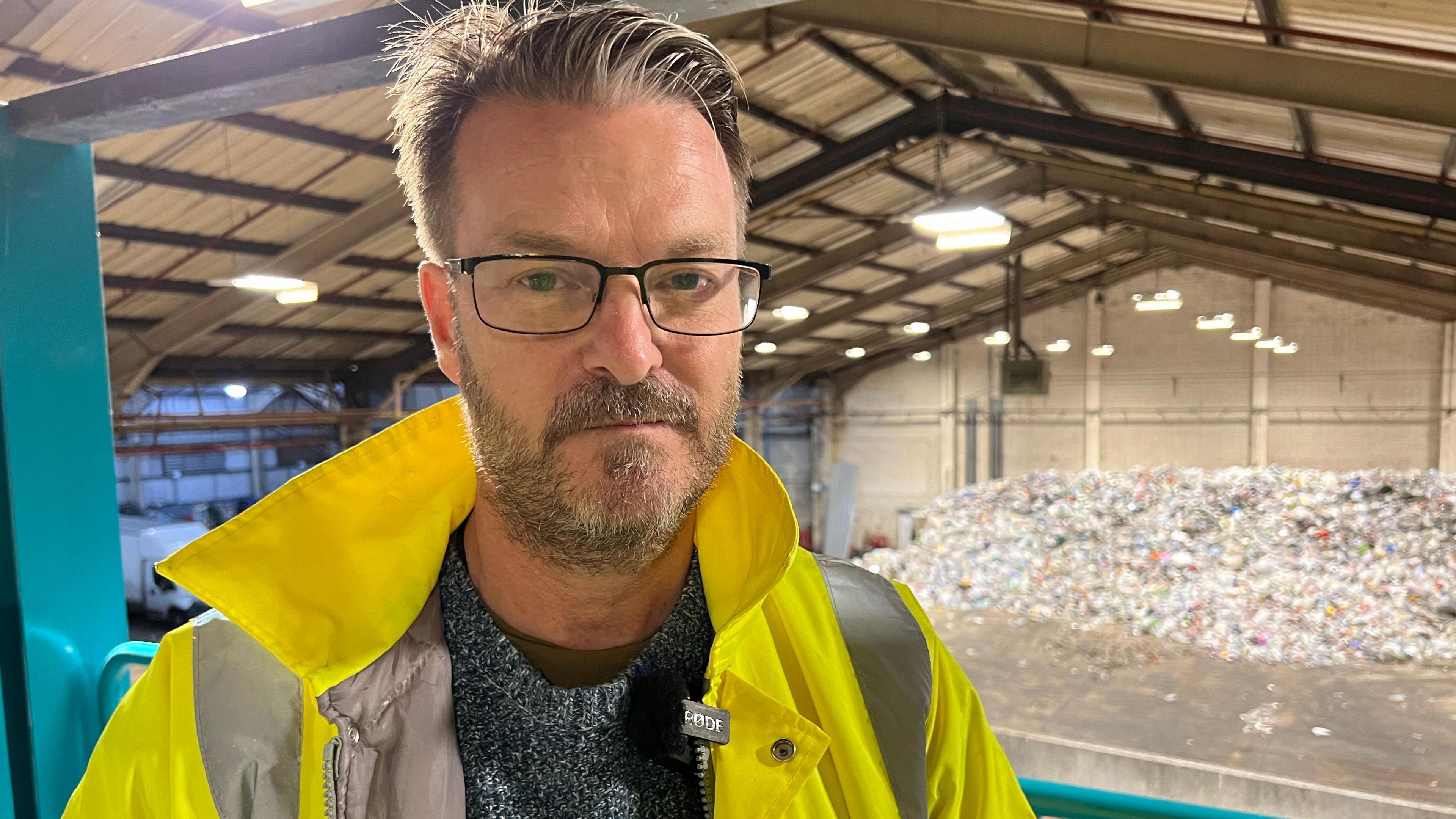 Councillor Chris Watts, cabinet member for the environment and transport stands in front of a mountain of waste at a recycling plant. 