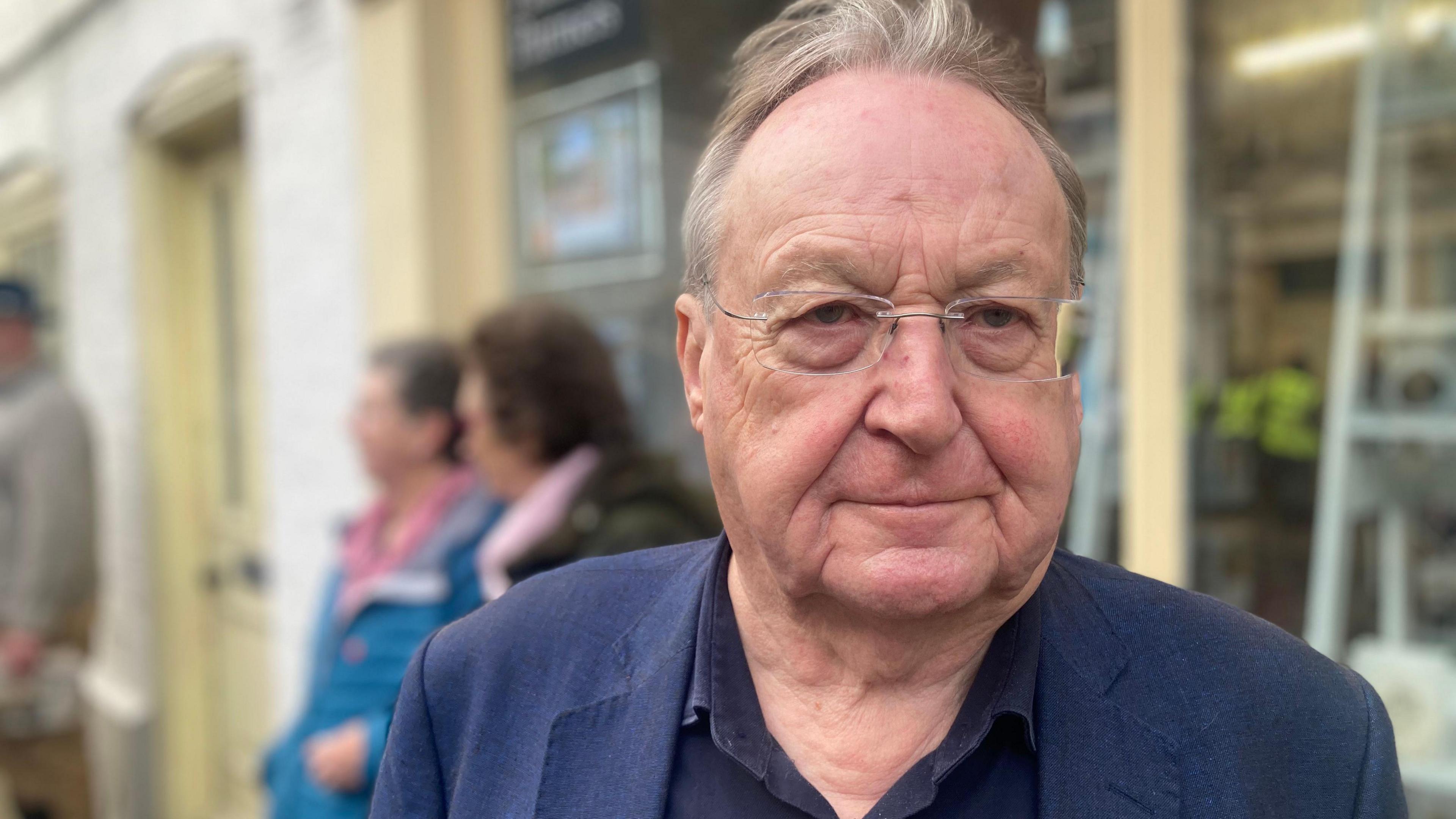 John Findlay wearing a dark blue shirt and a dark blue blazer, looking at the camera