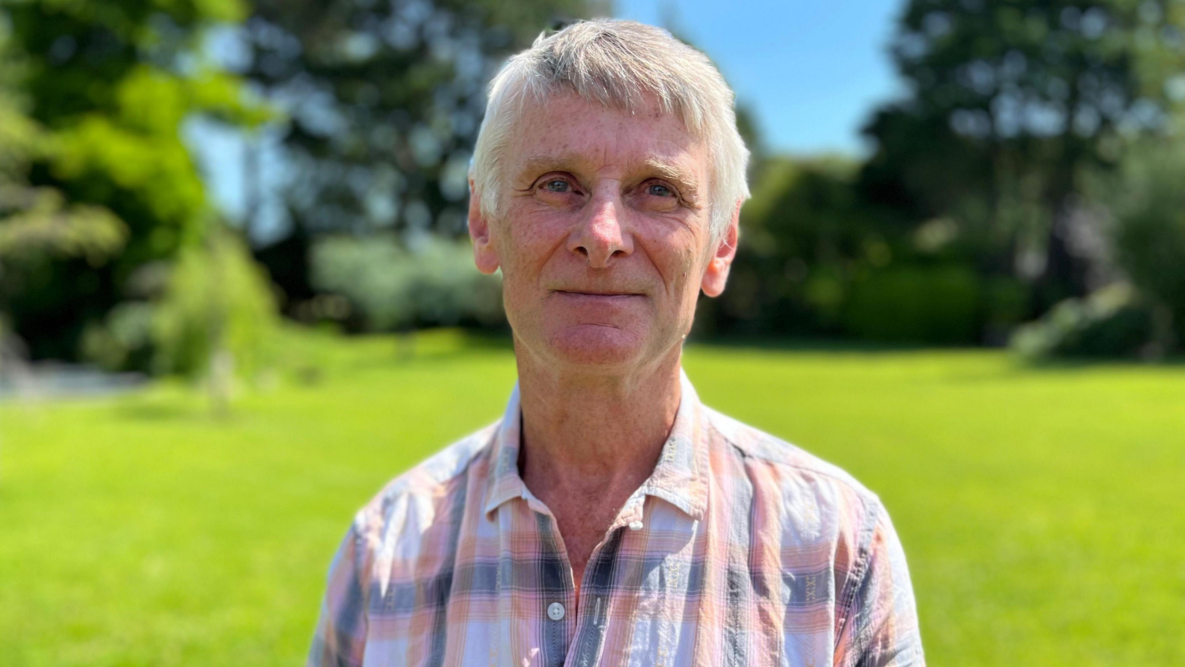 Jeff has short well kept silver/grey hair. He is wearing a salmon pink checked shirt.
