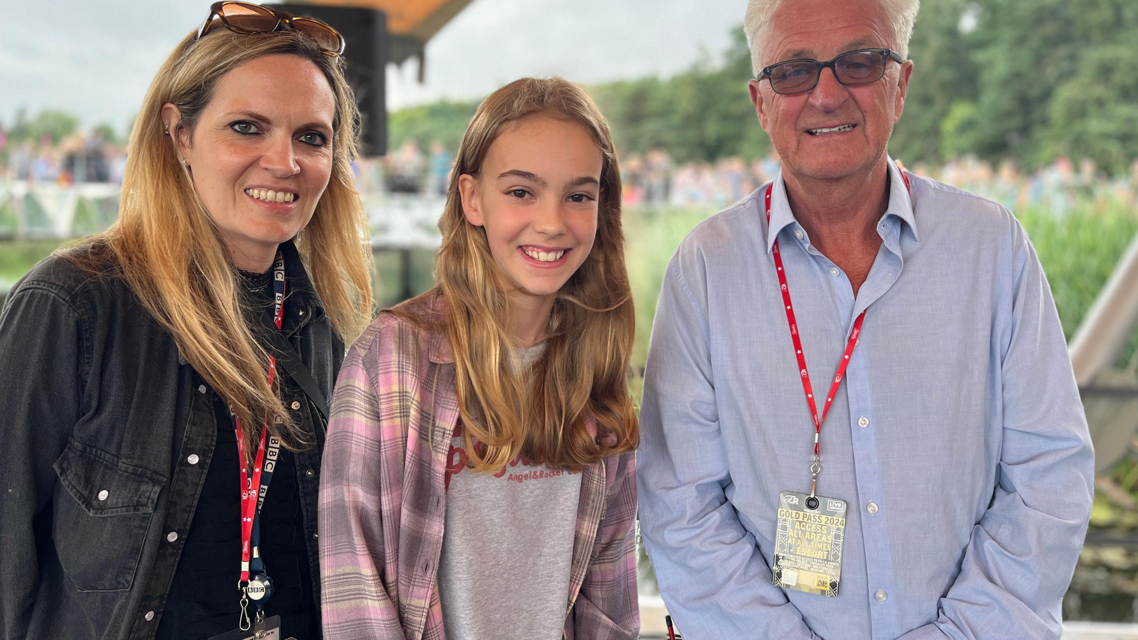 BBC Radio Suffolk's Sarah Lilley with long blonde hair and khol-rimmed eyes, Anna, with long blonde hair wearing a grey t-shirt and a pick plaid shirt and festival director Melvin Benn in a light blue shirt and short white hair and glasses standing on a stage