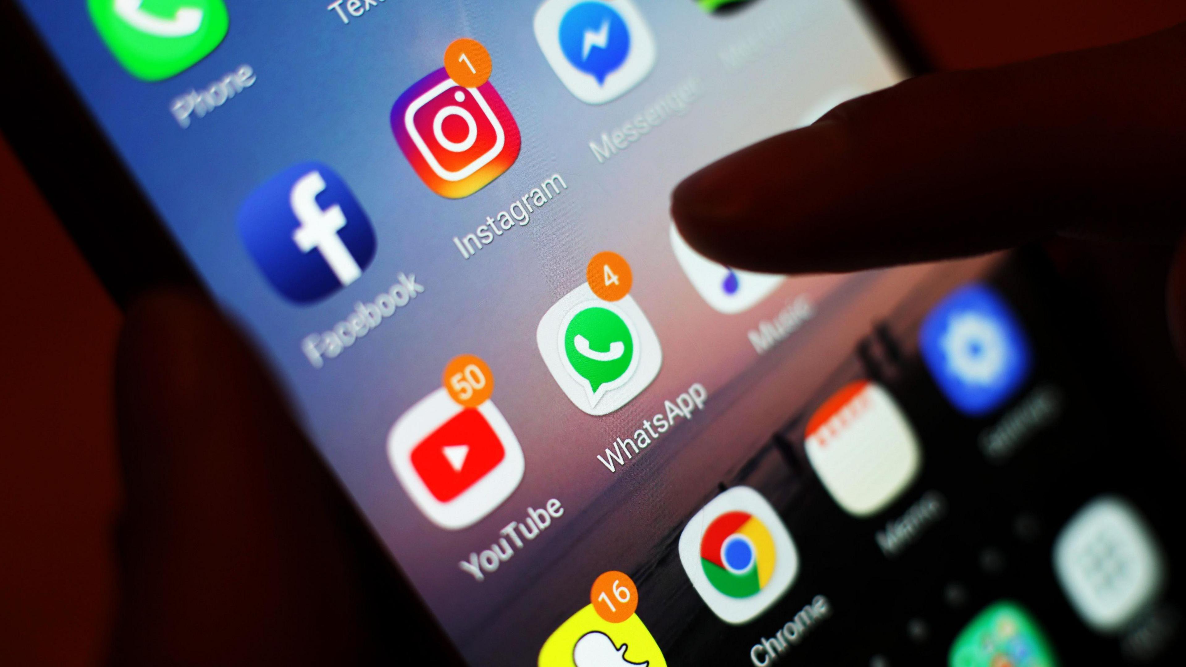 A mobile phone screen displaying several apps, with a silhouetted finger about to tap the WhatsApp icon.