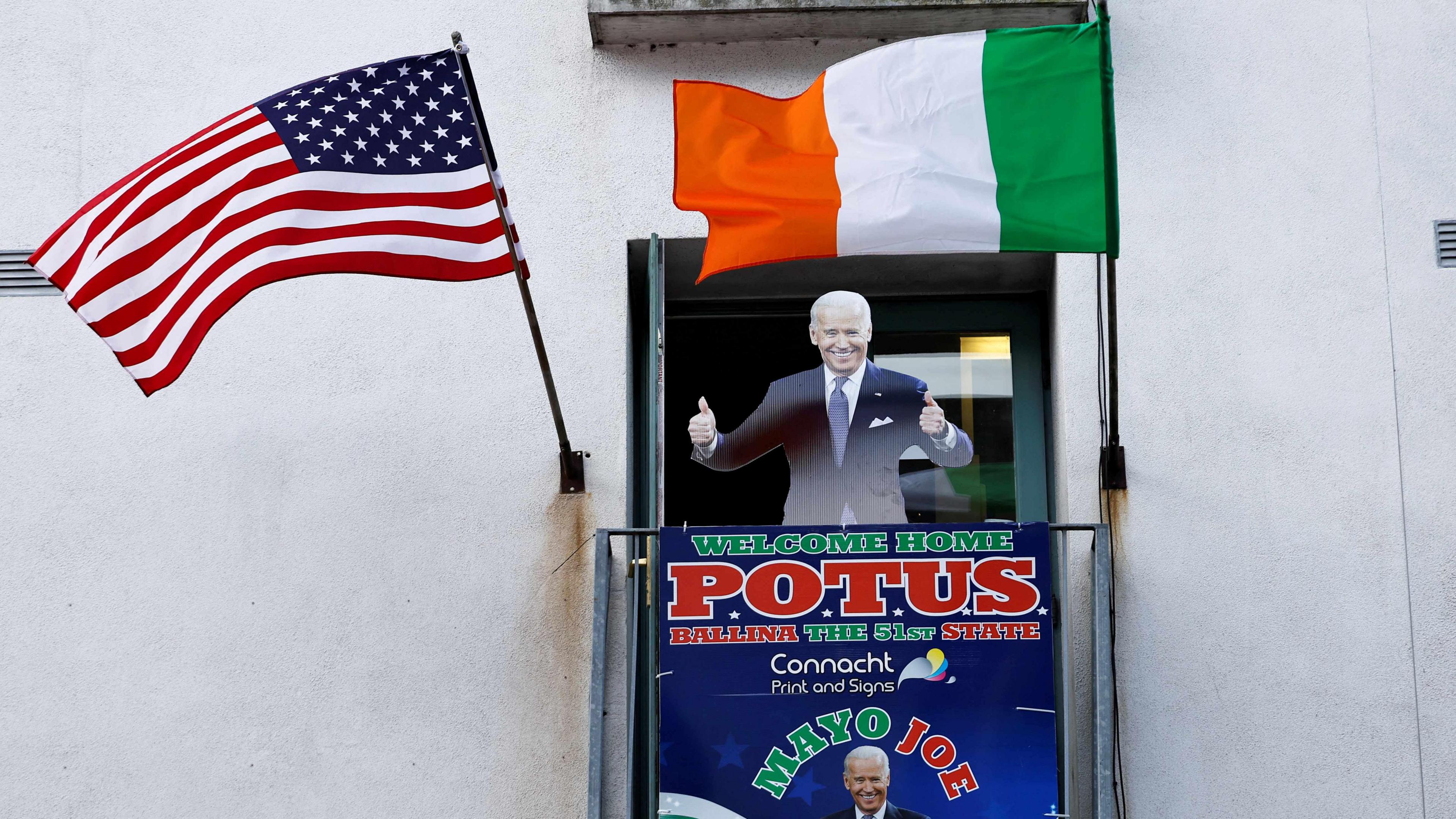 A cardboard cut-out of Joe Biden. Above the cut-out there is an Irish flag and an American flag. There is also a sign which reads 'WELCOME HOME POTUS'