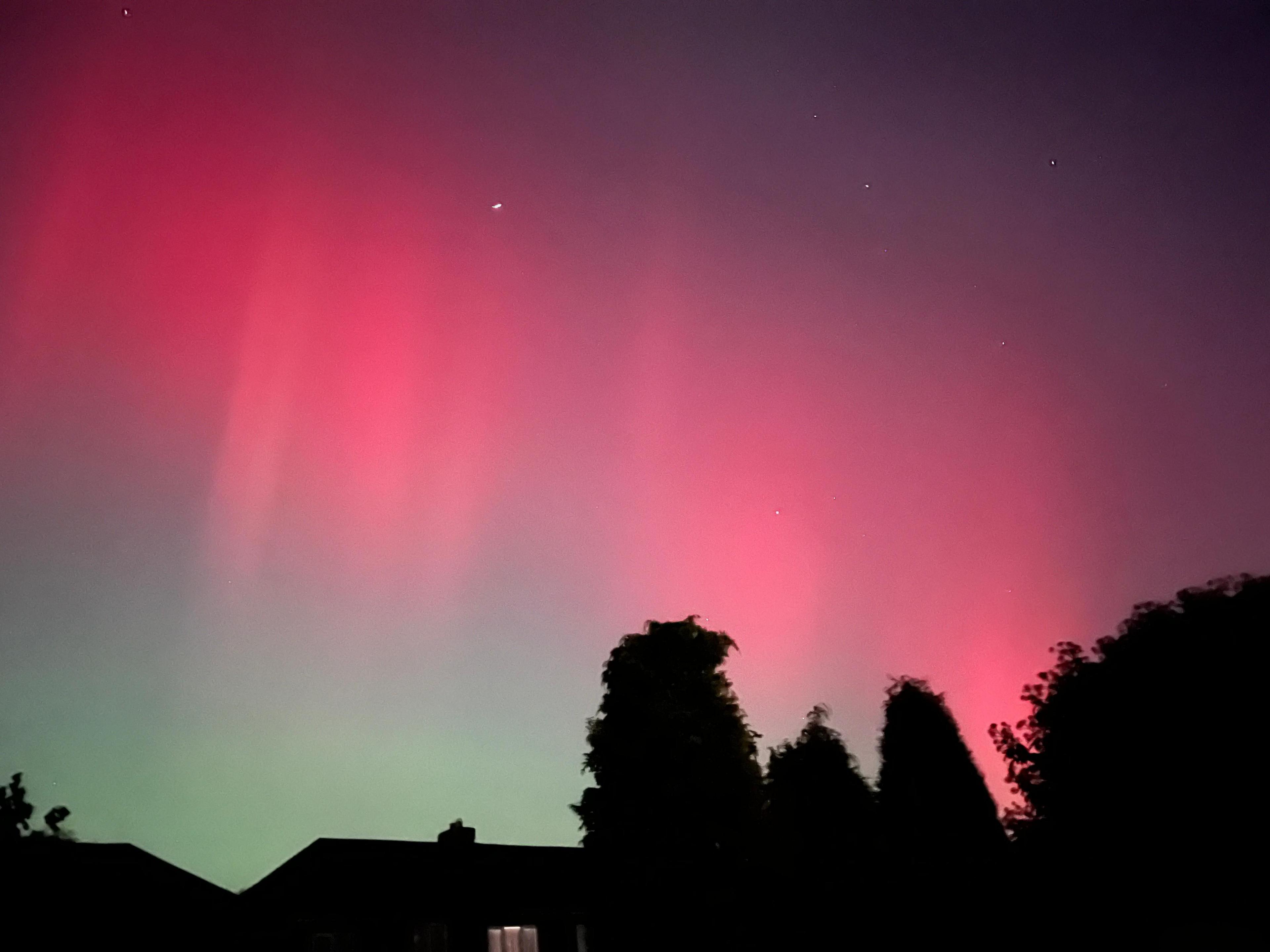 Splashes of red smudge the sky, with a house and trees in silhouette below