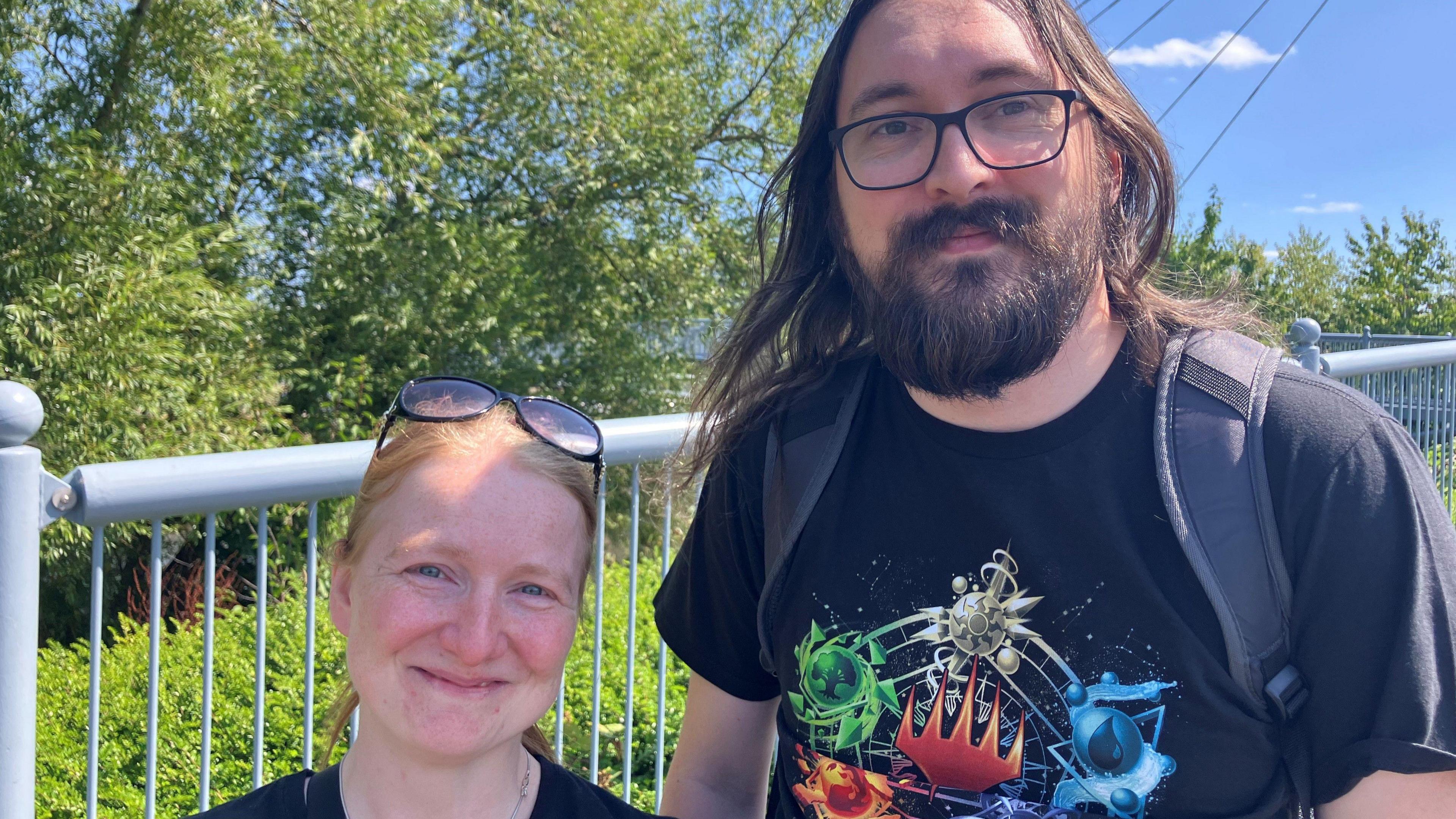 Jade Churchill and Craig Betham stand together on Worcester's Sabrina bridge on a sunny day. Both are wearing glasses and black T-shirts