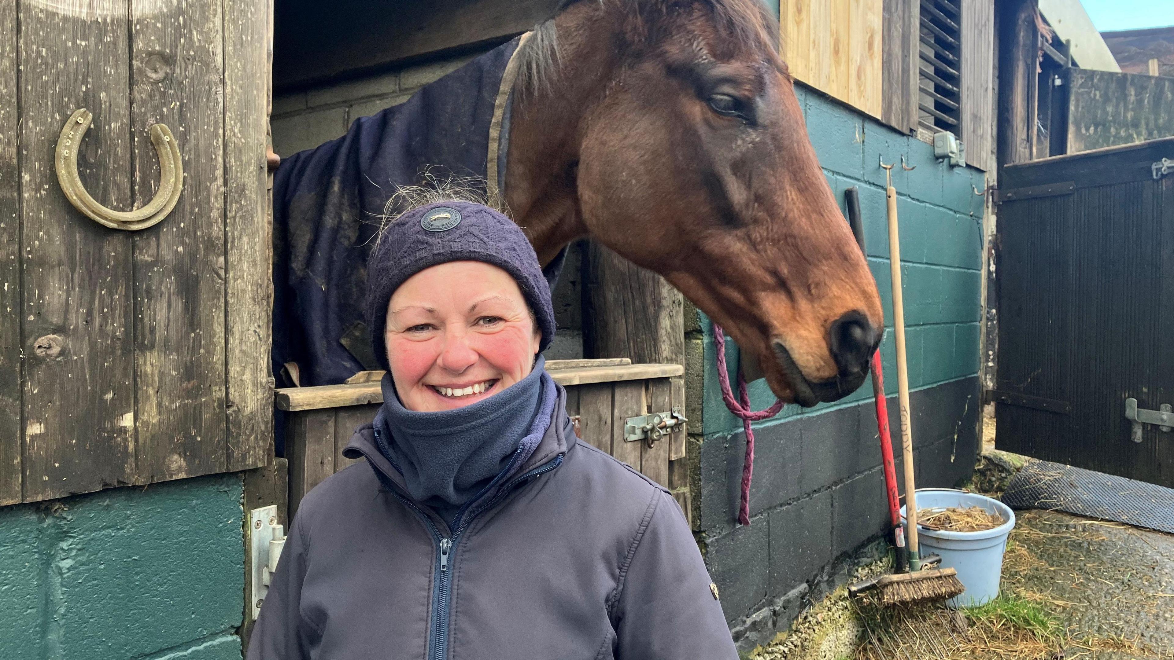 Photograph of Inga Hulme and a horse, in front of stables at the farm where she lives.