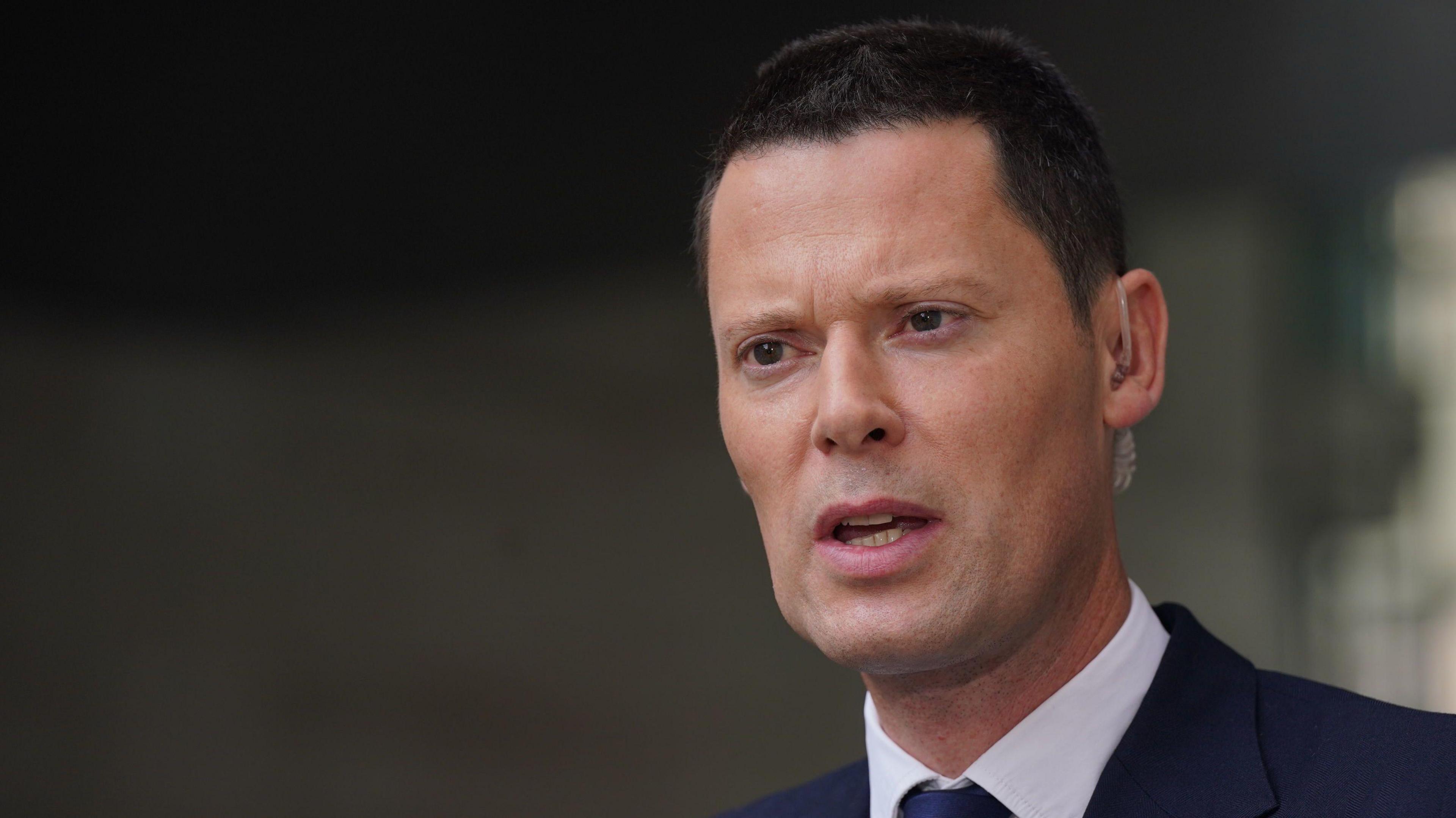 Alex Chalk speaking to the press. The head and shoulders or Mr Chalk are pictured as he looks to the side of the camera and he is wearing a shirt, tie and jacket. 