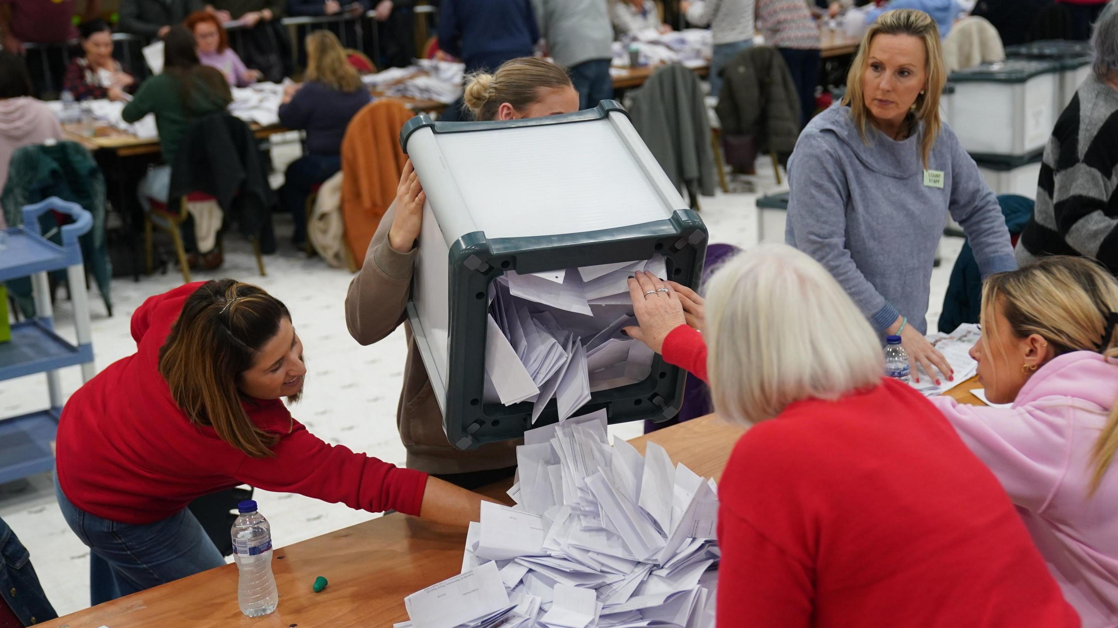 A woman empties a box full of ballot papers onto a table at an election count in Cork. Four other women look on as they prepare to count the ballots.