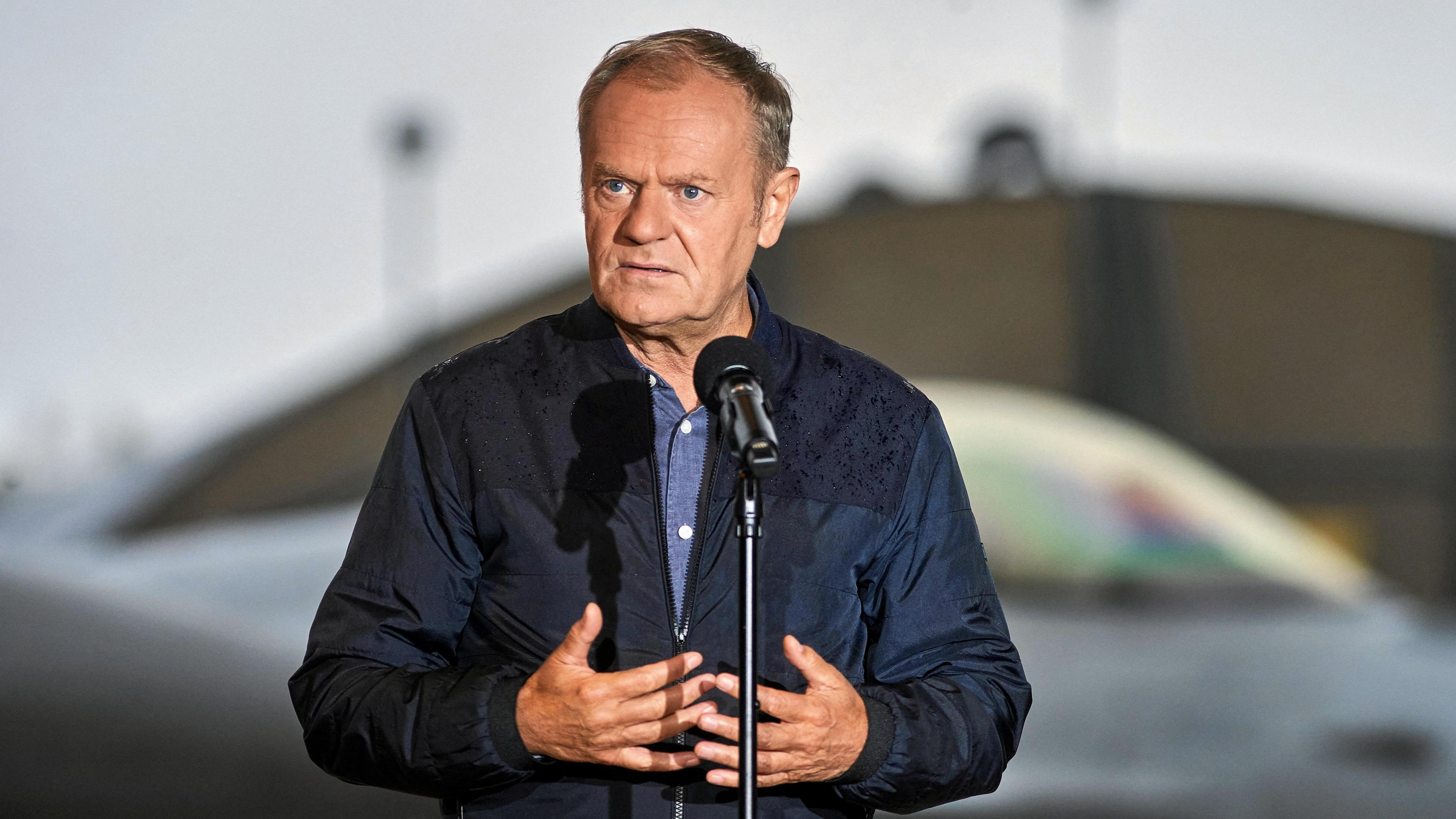 A man in a navy jacket stands in front of a microphone