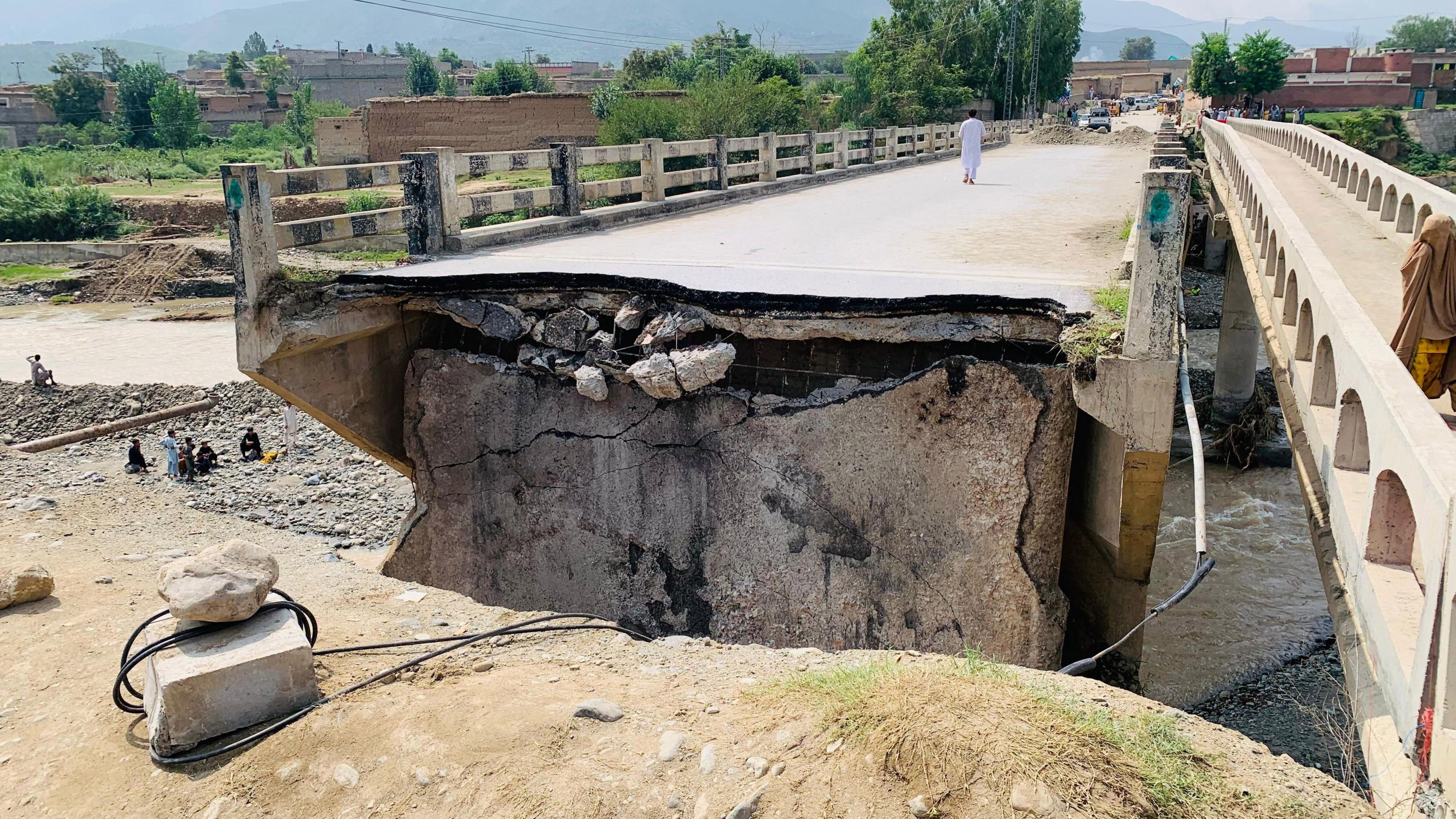A view of a damaged bridge following flash floods and torrential rains, in Bajaur, KPK province, Pakistan, 17 August 2025. There is a gap between the land and the concrete bridge, a man in white is walking away from the gap.