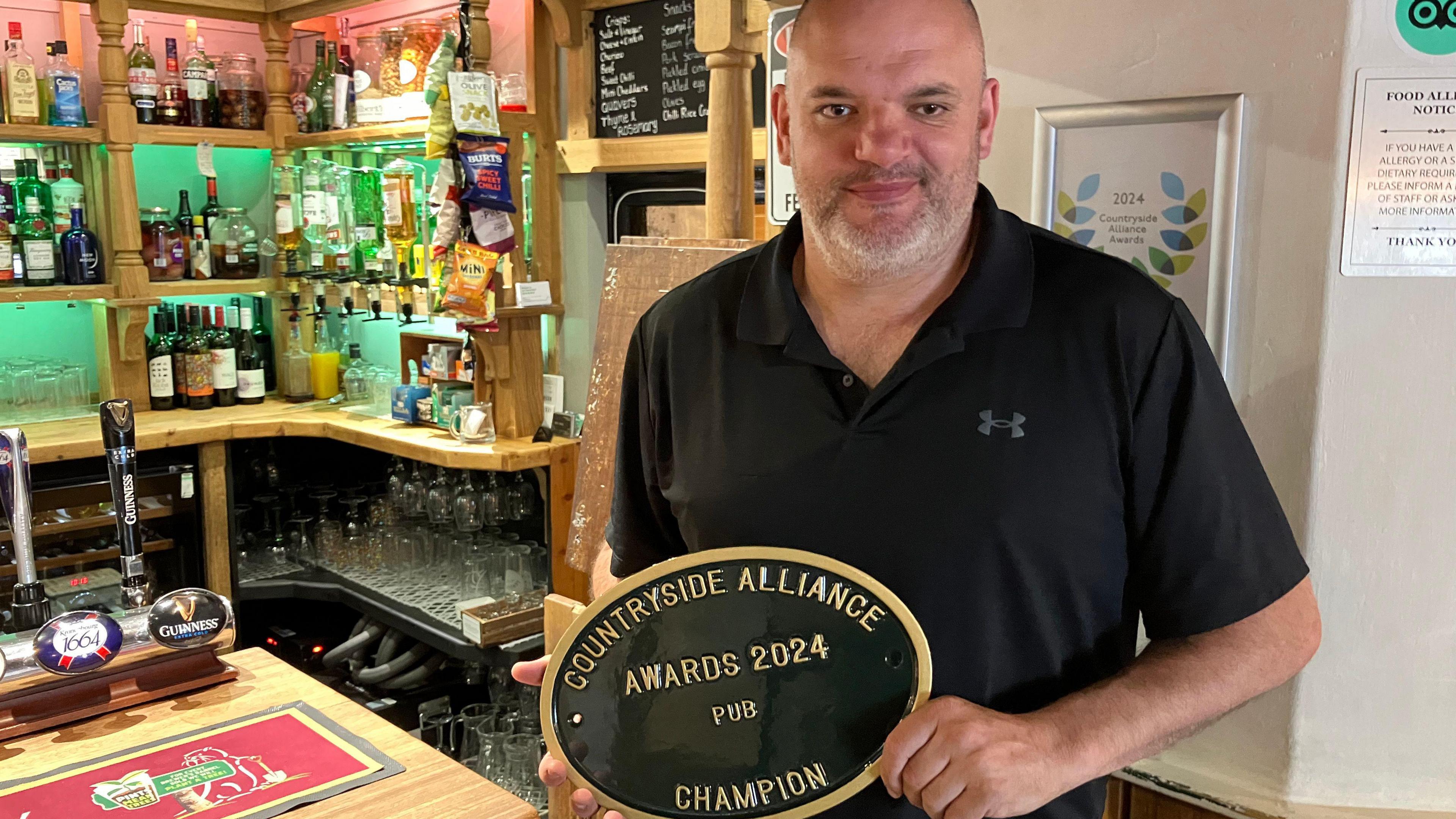 Photo of Dan Prettejohn holding the award plaque next to his bar