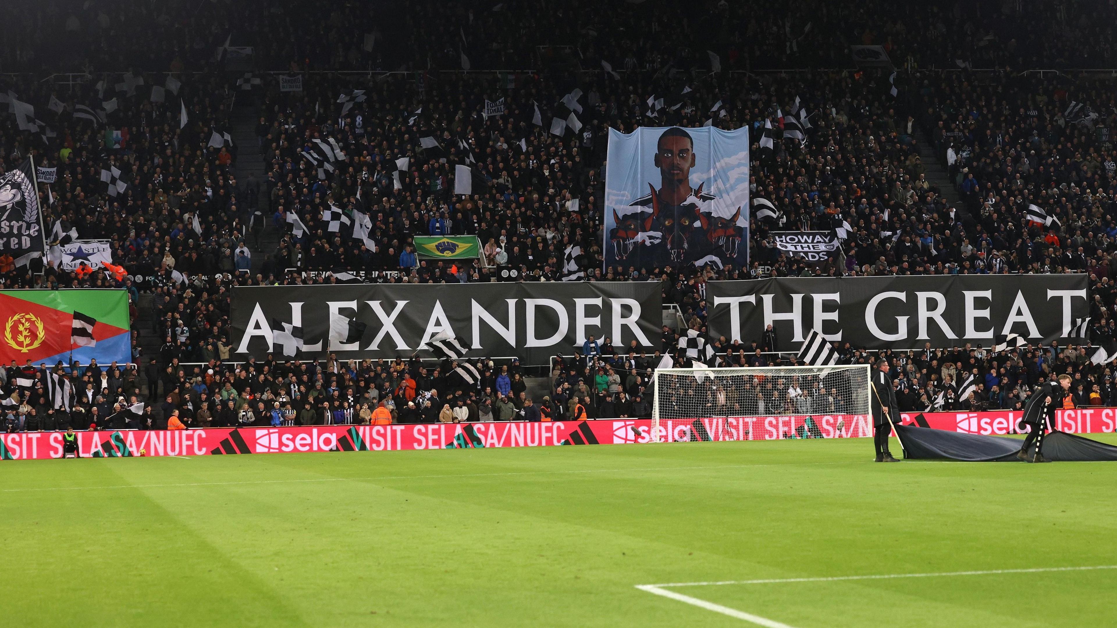 Newcastle United fans in the Gallowgate End display an Eritrean flag, a picture of Alexander Isak and a sign in black and white reading 'Alexander the Great' in reference to the striker, with a largely empty pitch in the foreground