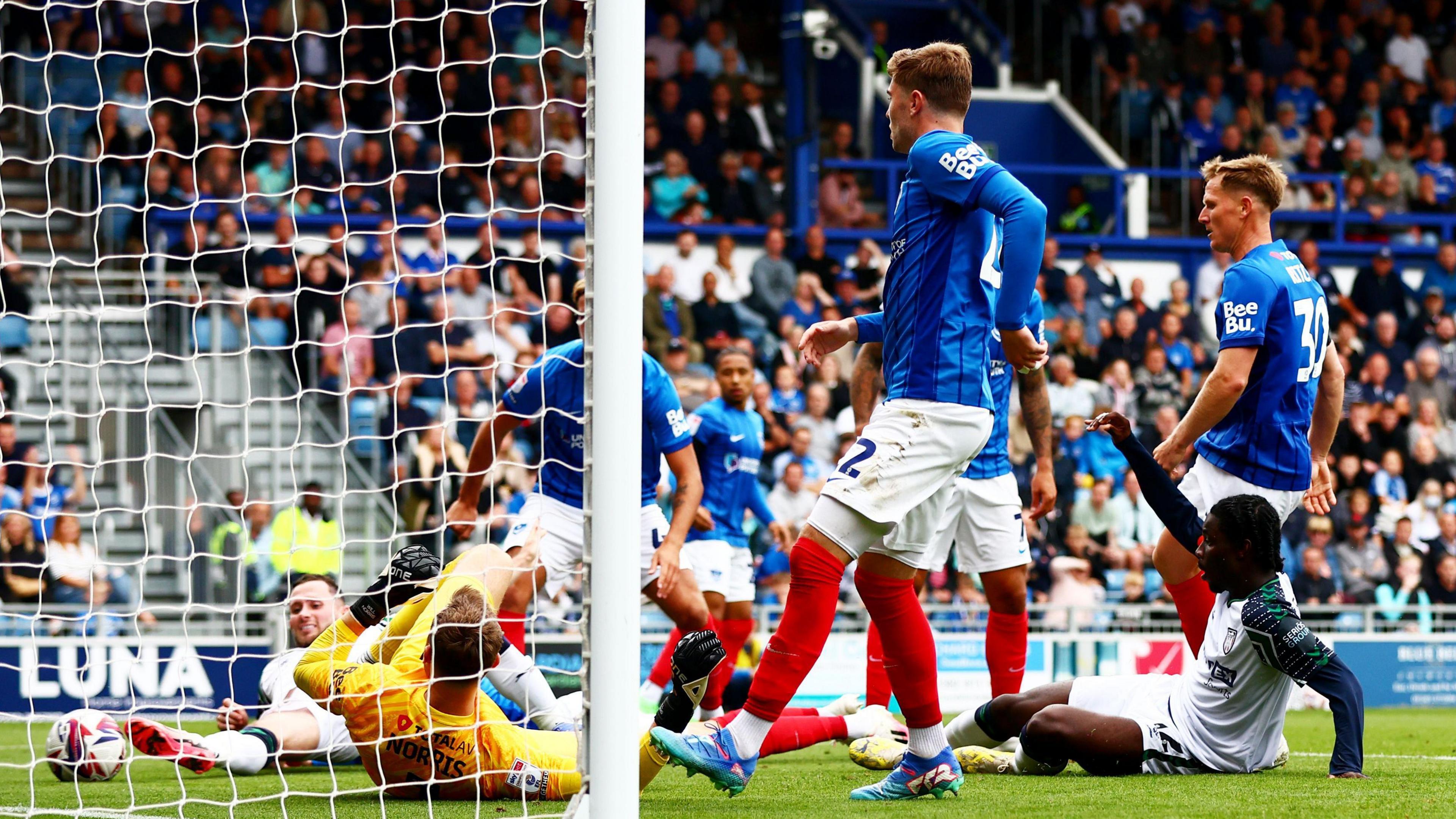 Eliezer Mayenda is on the ground in front of goal as he celebrates scoring for Sunderland against Portsmouth and is surrounded by opposition players.