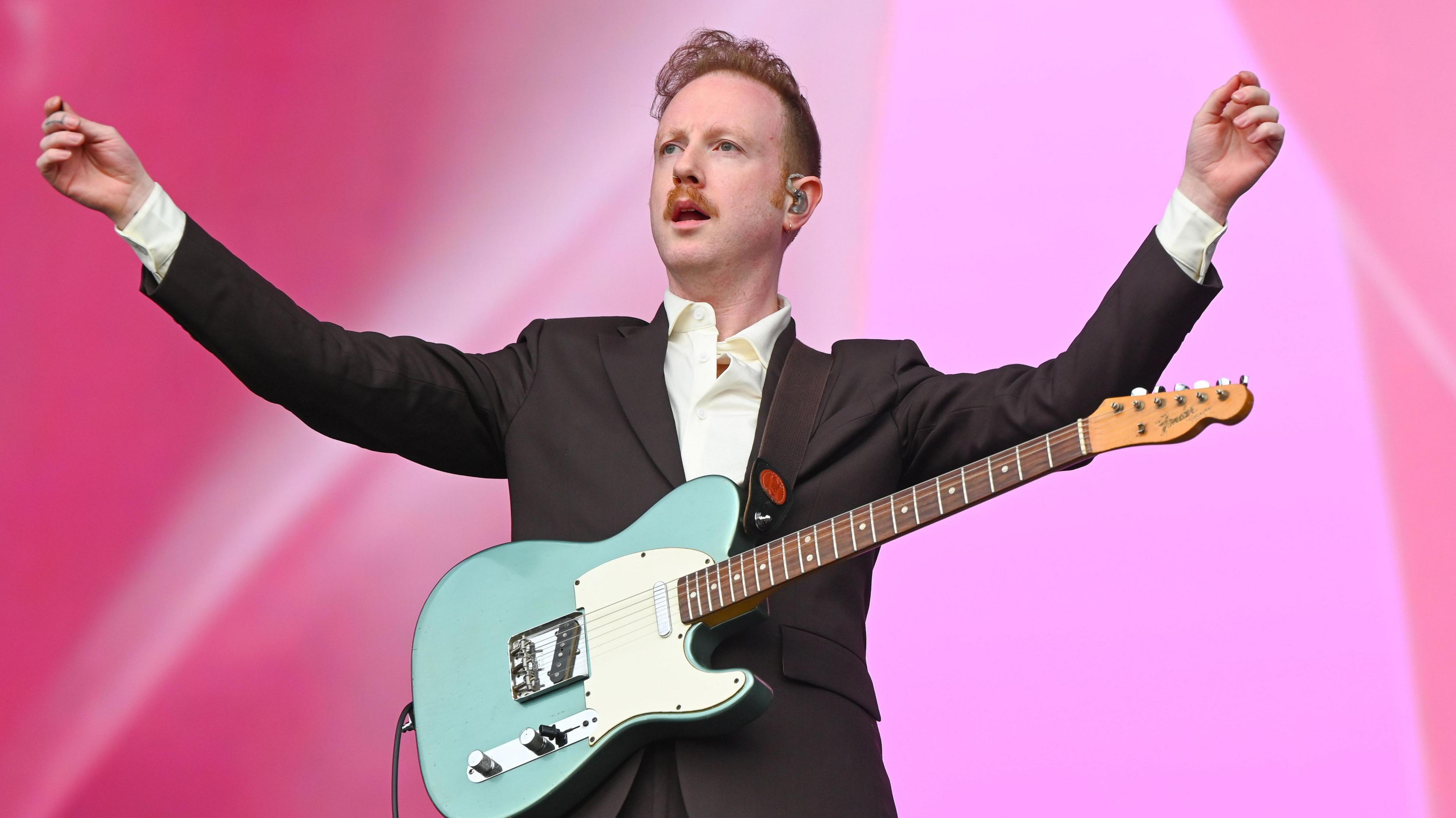 Alex Trimble from Two Door Cinema Club is on stage with his guitar, his arms aloft.