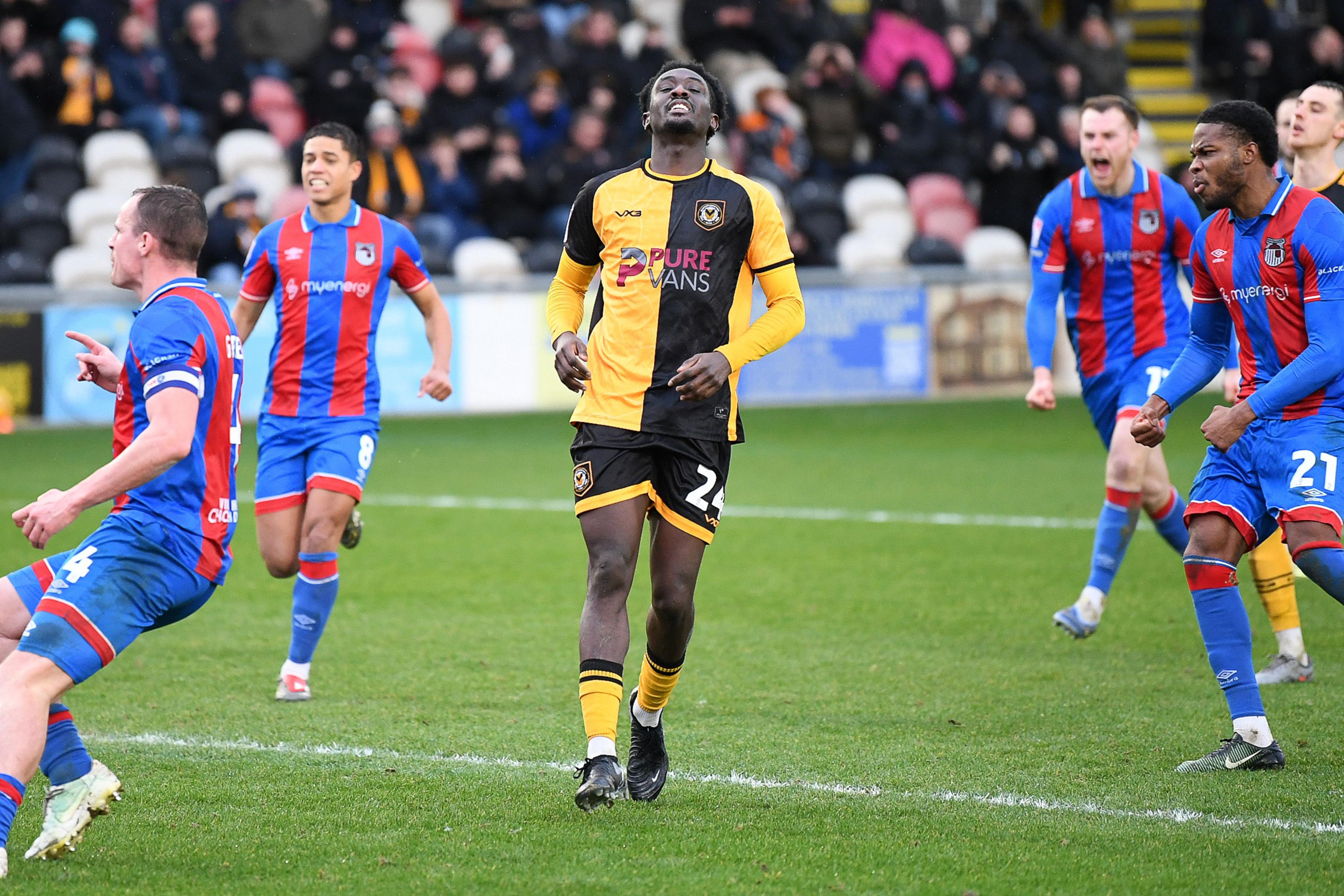 Nathaniel Opoku rodeado de jugadores de Grimsby después de fallar un penalti para Newport County