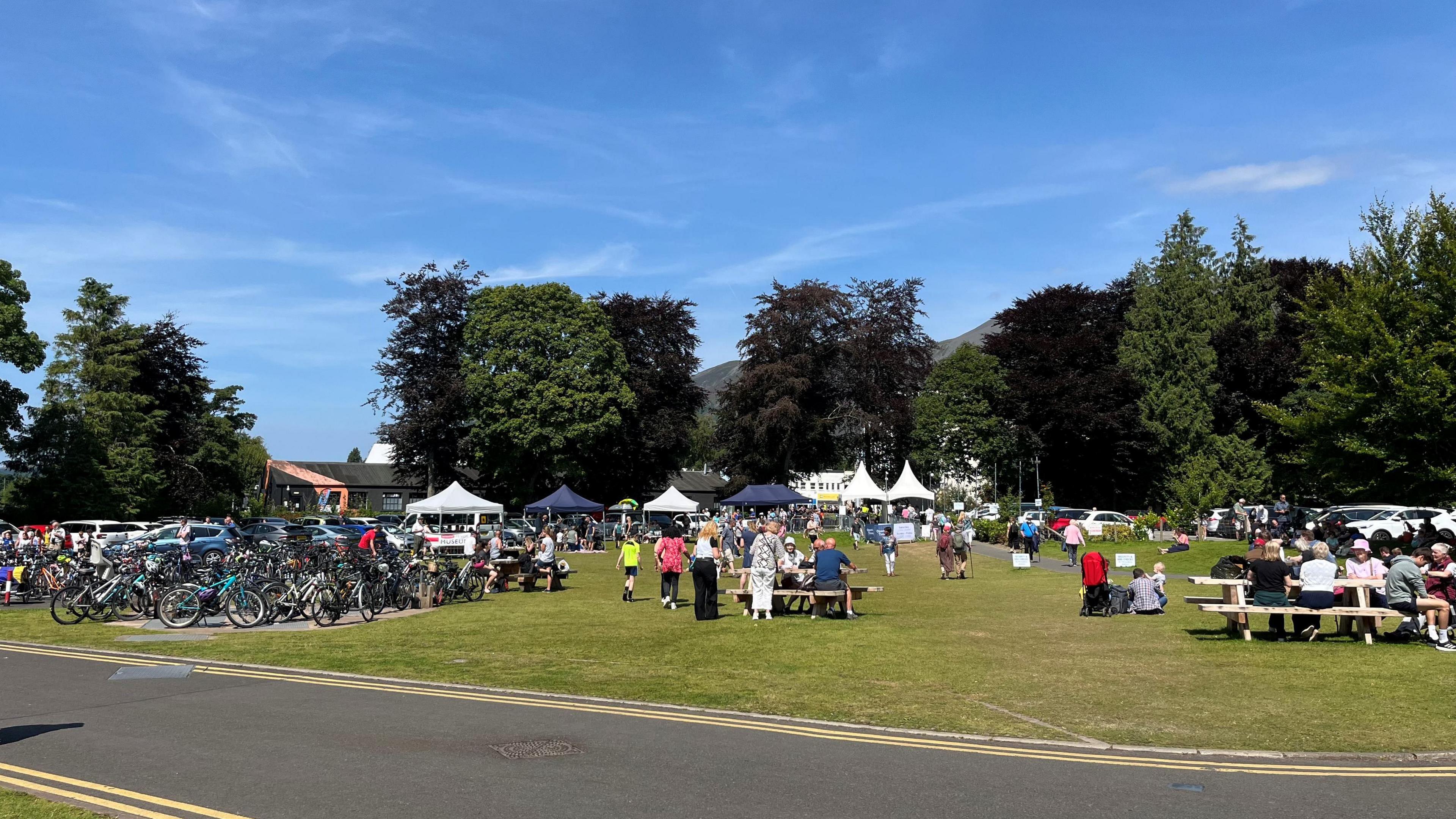 People sat on picnic tables with the Keswick convention gazebos in the background.