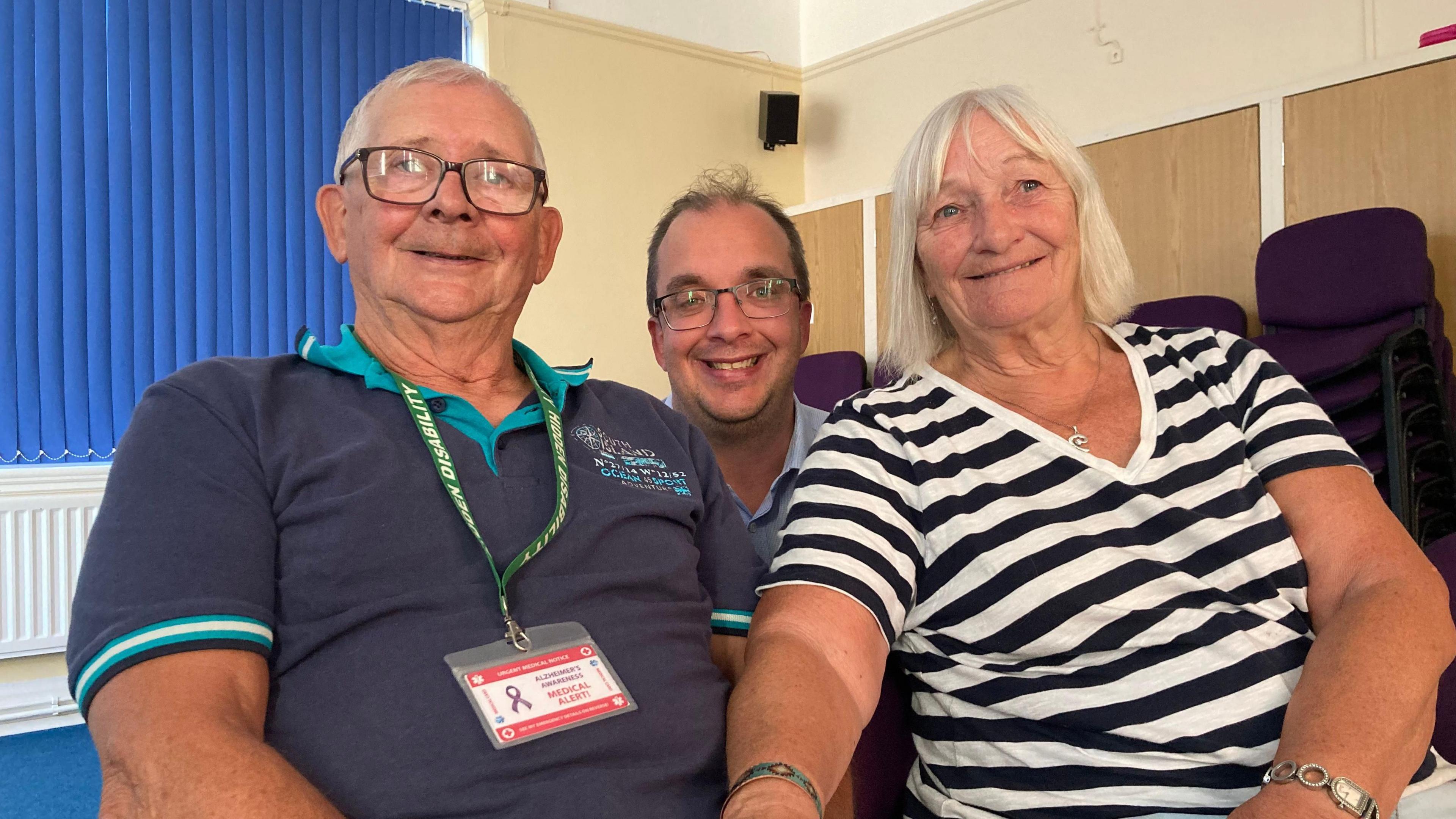 Graham has short grey hair and glasses, he is wearing a green and navy polo shirt, and a green hidden disability lanyard. Rick has short dark hair and glasses. Lorraine has short blonde hair and is wearing a black and white striped top.