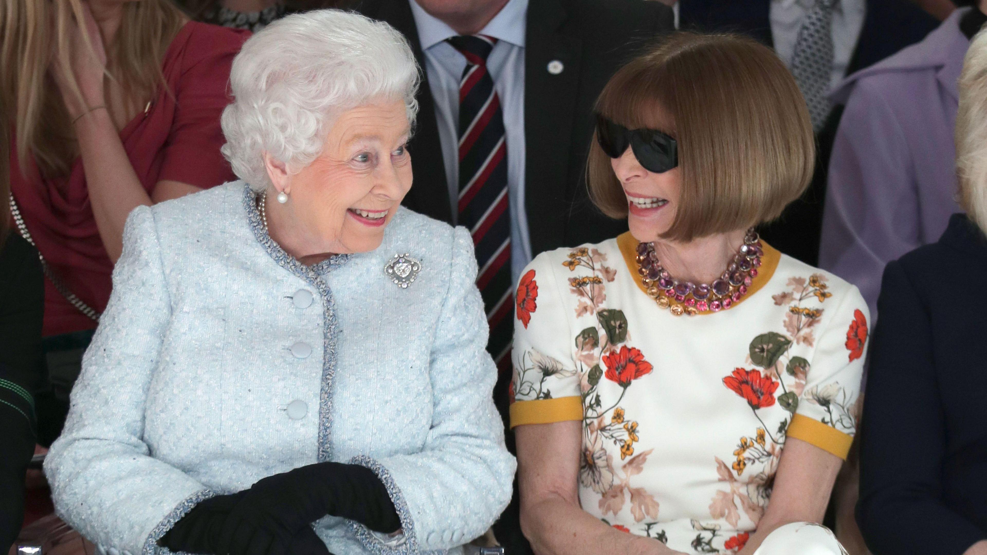 Queen Elizabeth II and Anna Wintour sitting next to each other and smiling at a fashion show in london in 2018